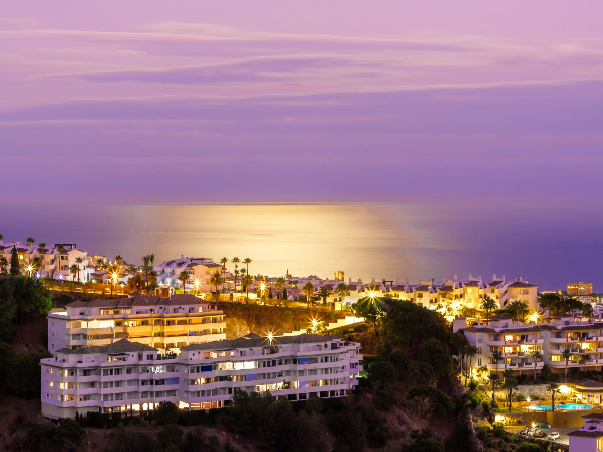 Illuminated coastal resort at twilight with palm trees and ocean view.