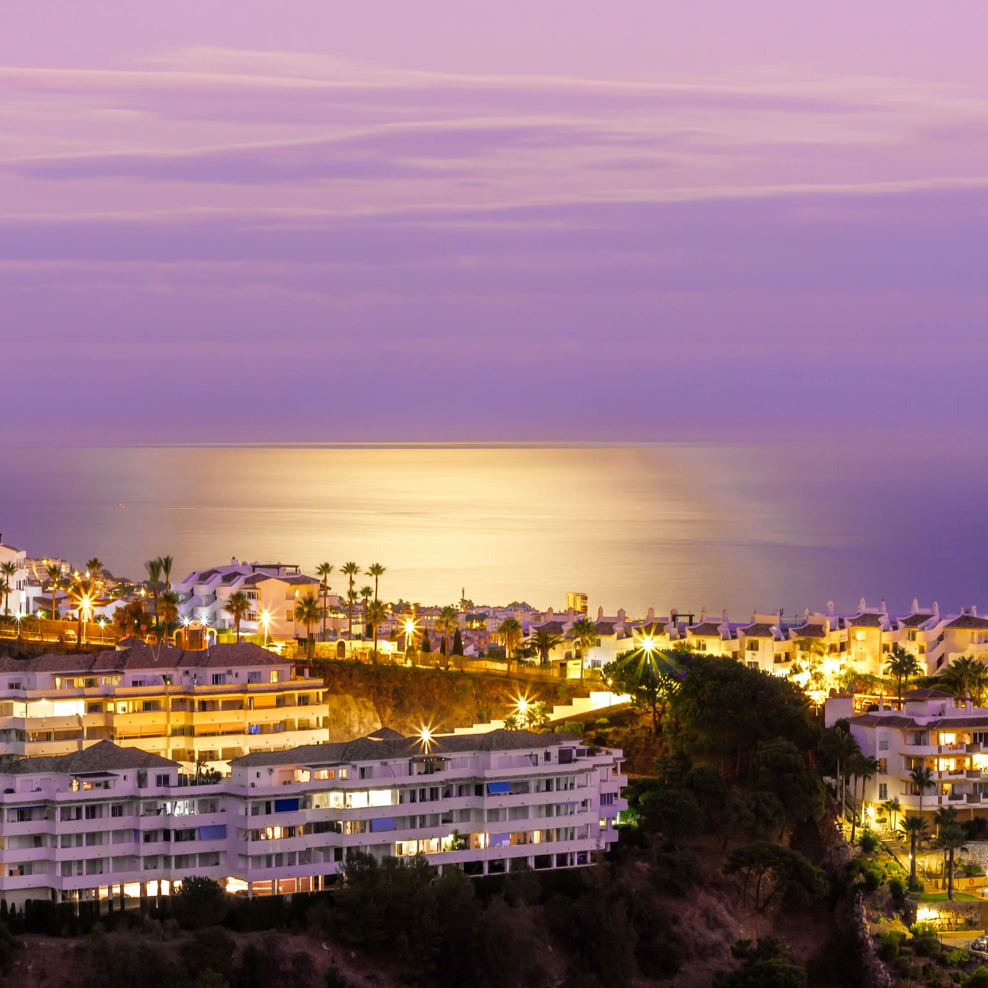 Illuminated coastal resort at twilight with palm trees and ocean view.