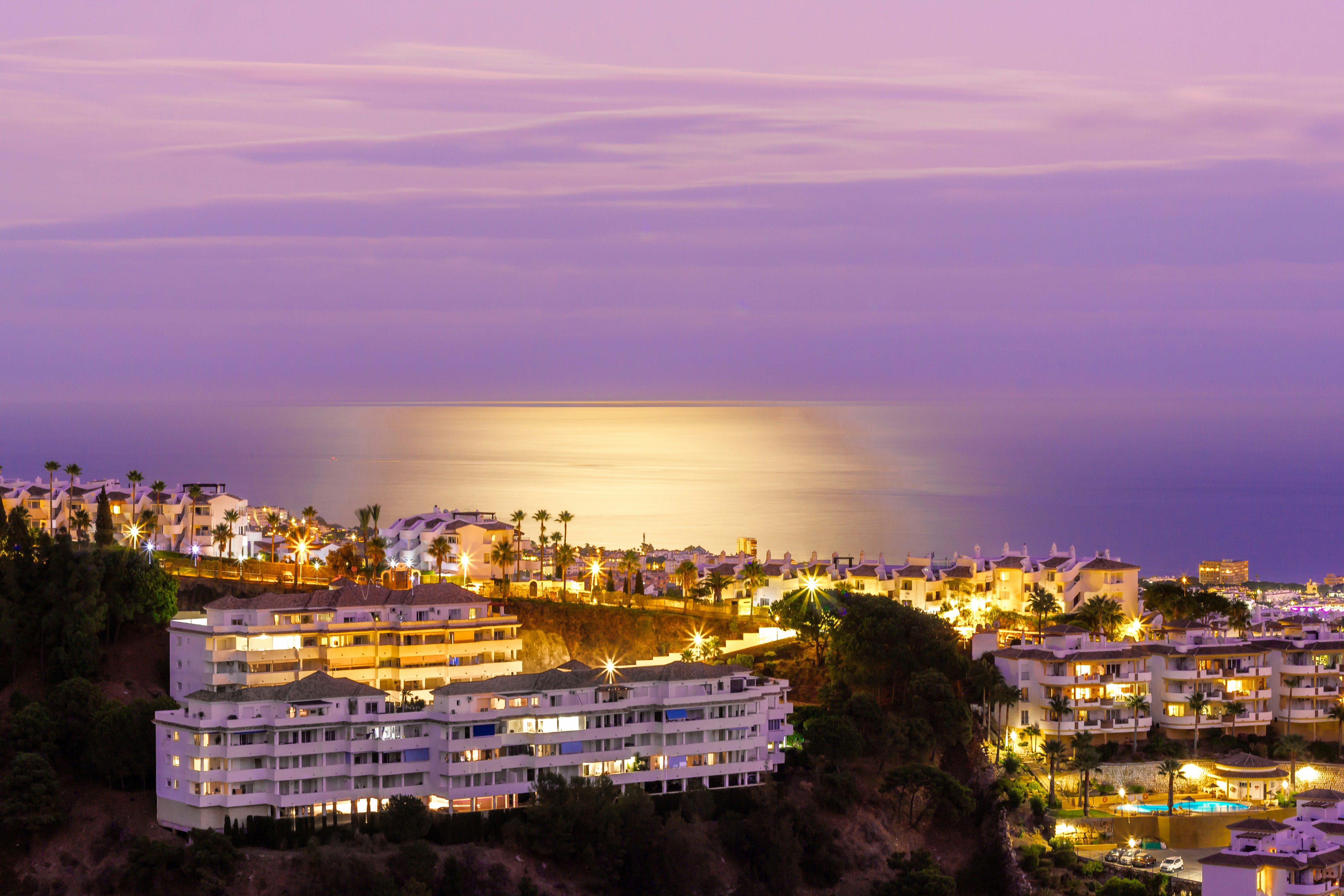 Illuminated coastal resort at twilight with palm trees and ocean view.