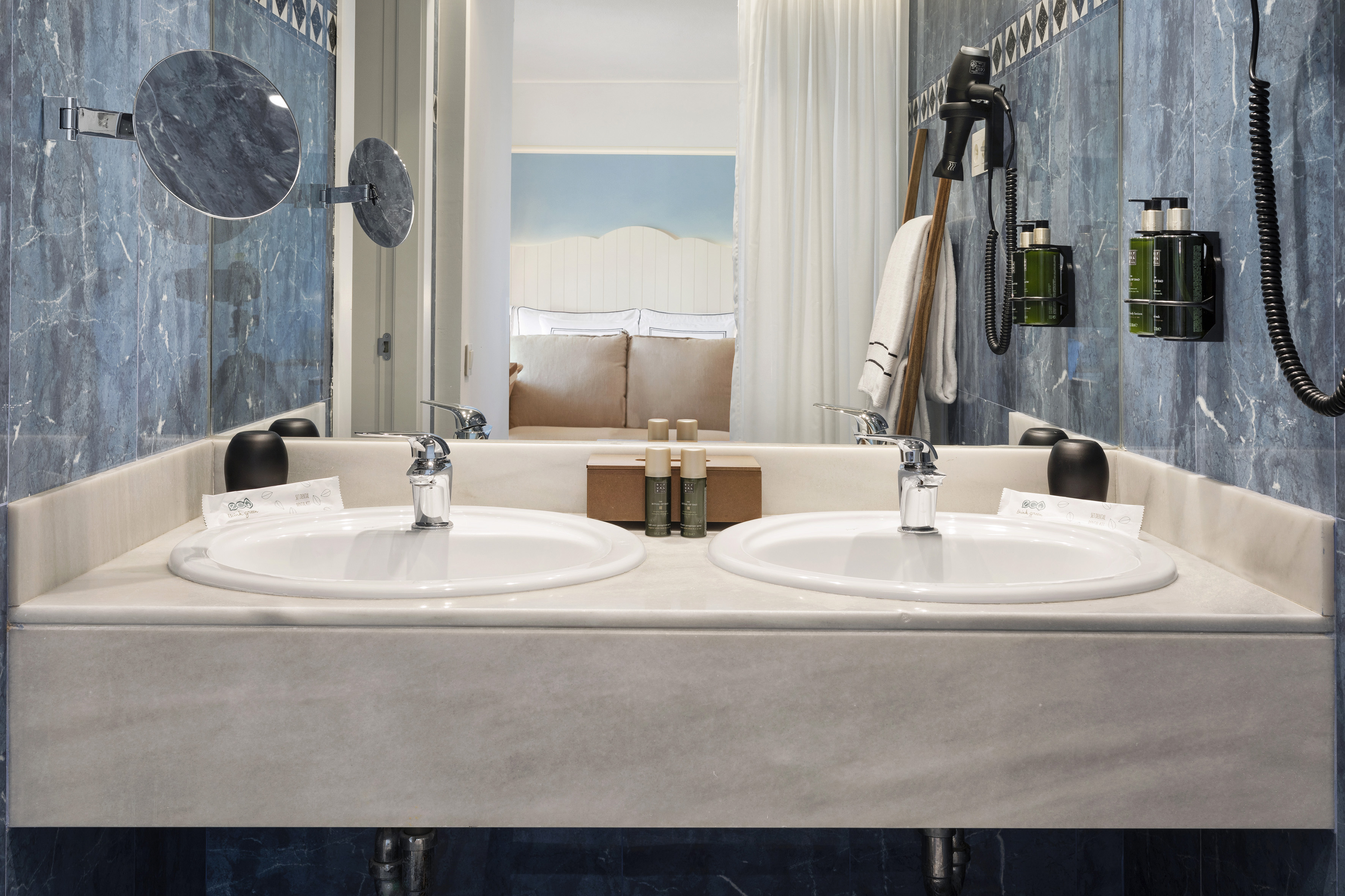 Hotel bathroom with double vanity, blue marble walls, modern chrome fixtures.