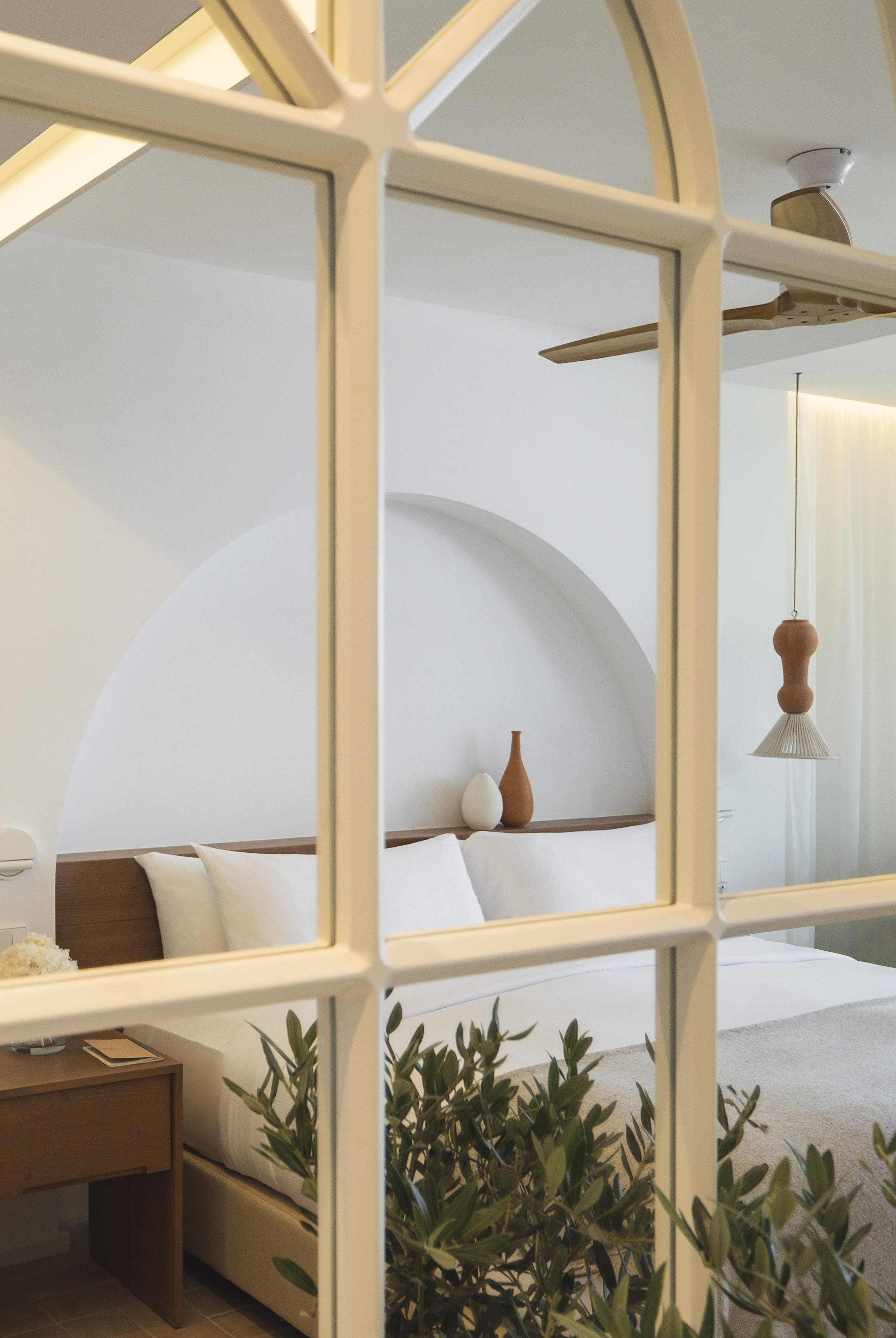Minimalist white bedroom with arched alcove, wooden bed, hanging lamp, olive branches.