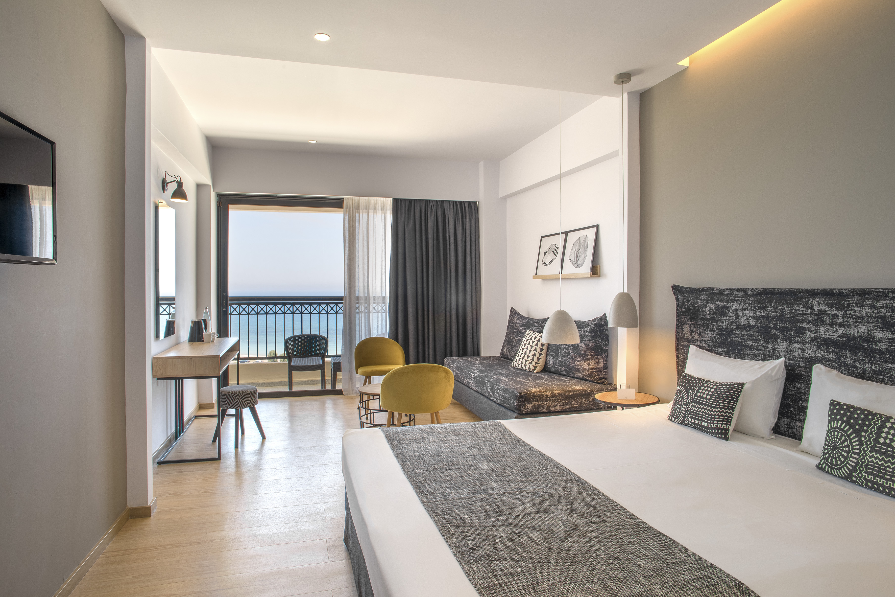 Modern hotel room with balcony sea view, large bed, and seating area.