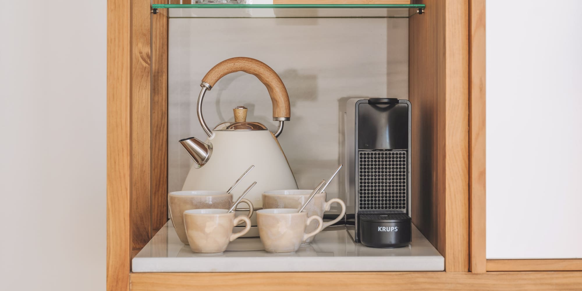 Hotel coffee and tea station with kettle, Krups machine, ceramic mugs.