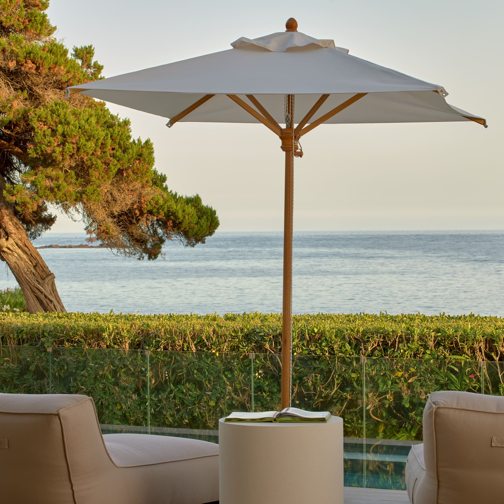 Ocean view patio with lounge chairs, umbrella, and lush coastal landscaping.