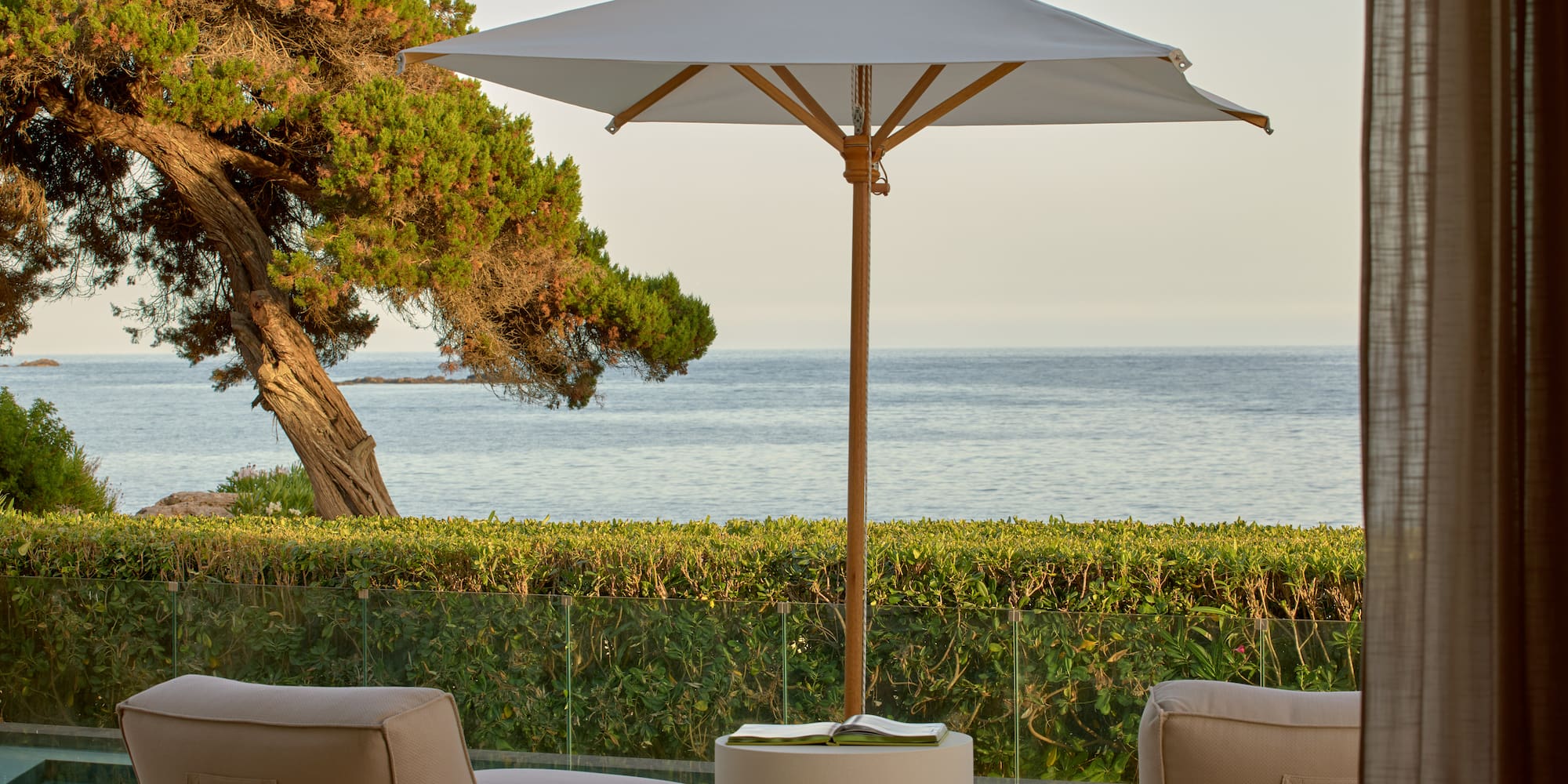 Ocean view patio with lounge chairs, umbrella, and lush coastal landscaping.