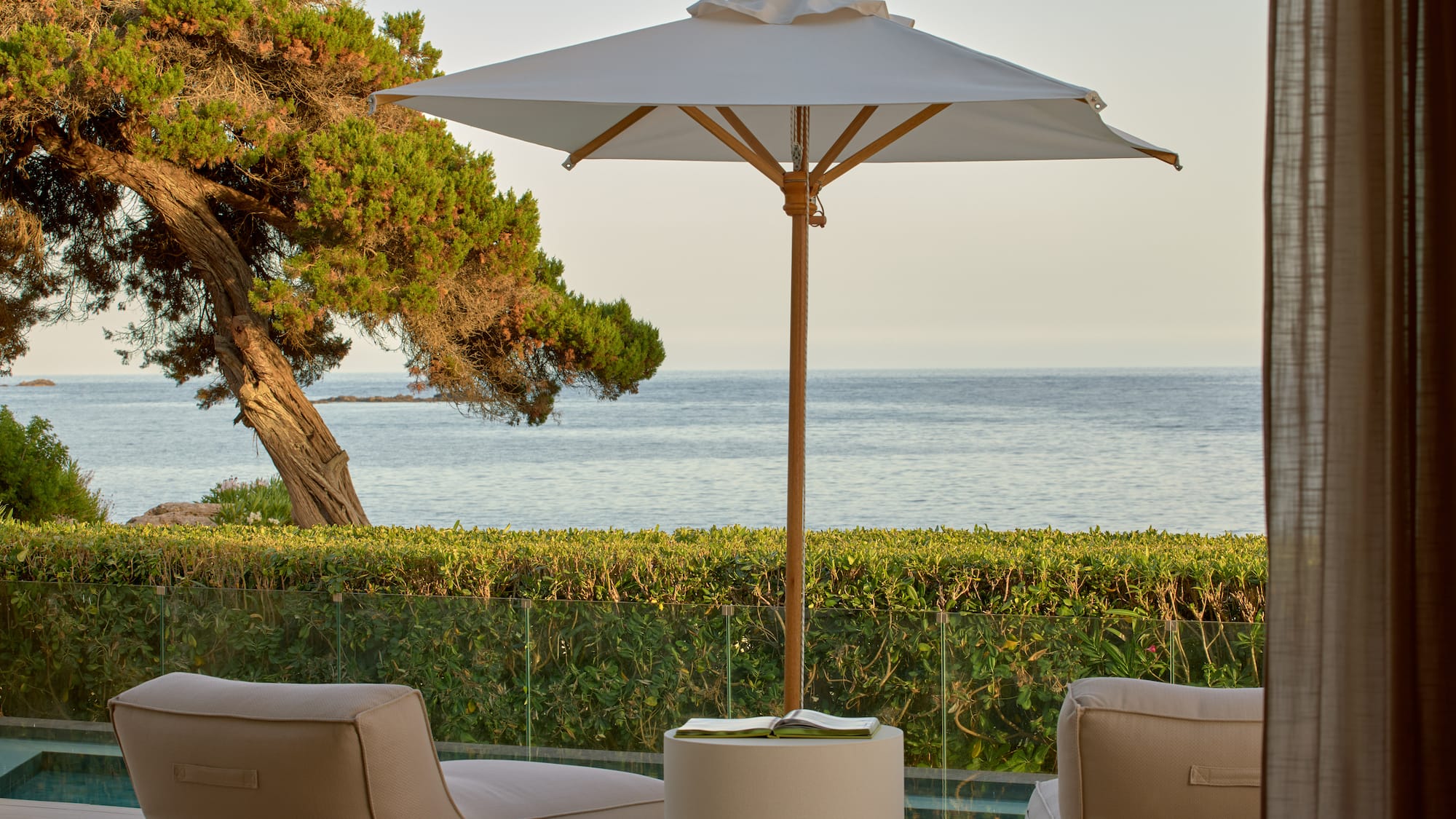 Ocean view patio with lounge chairs, umbrella, and lush coastal landscaping.