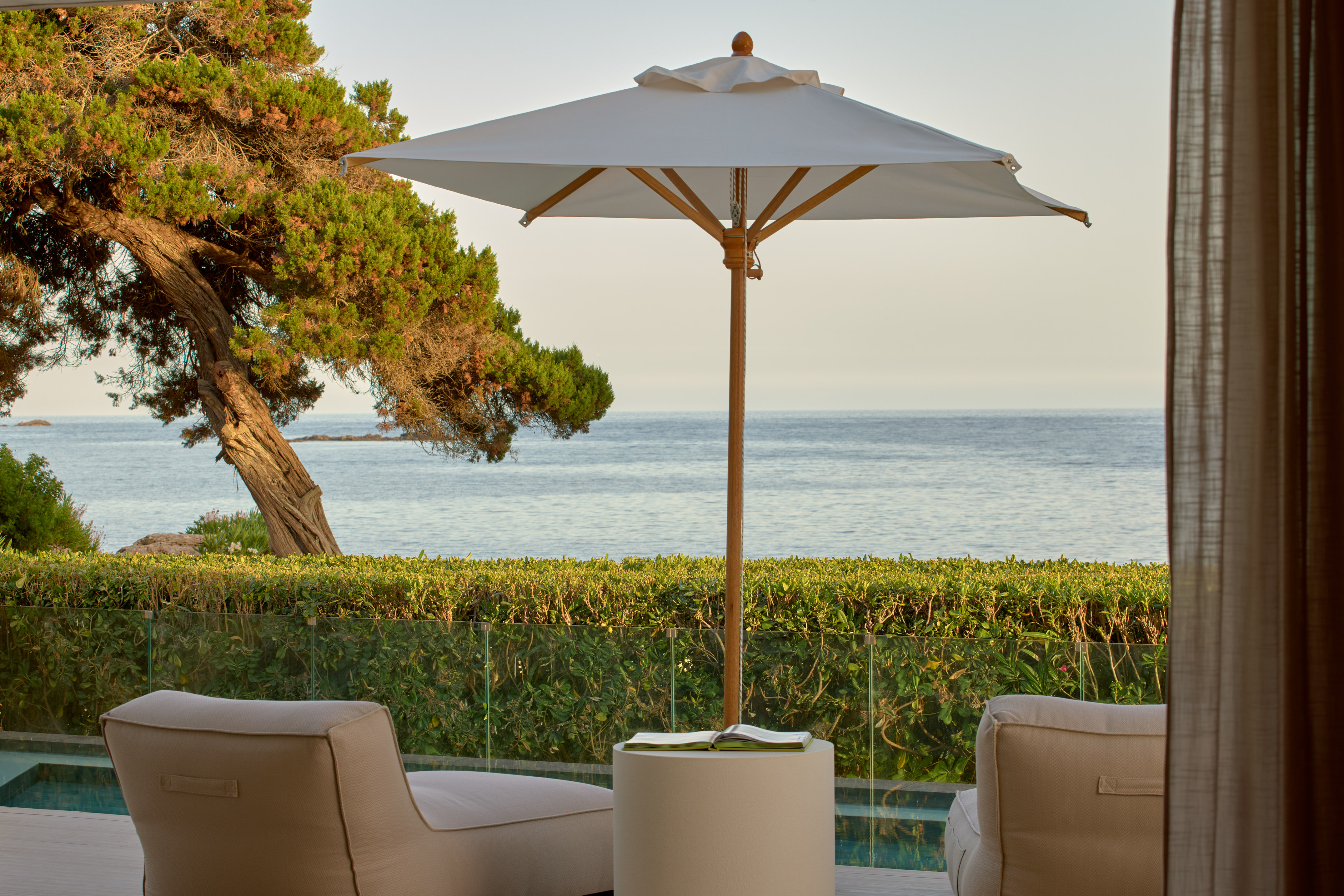 Ocean view patio with lounge chairs, umbrella, and lush coastal landscaping.