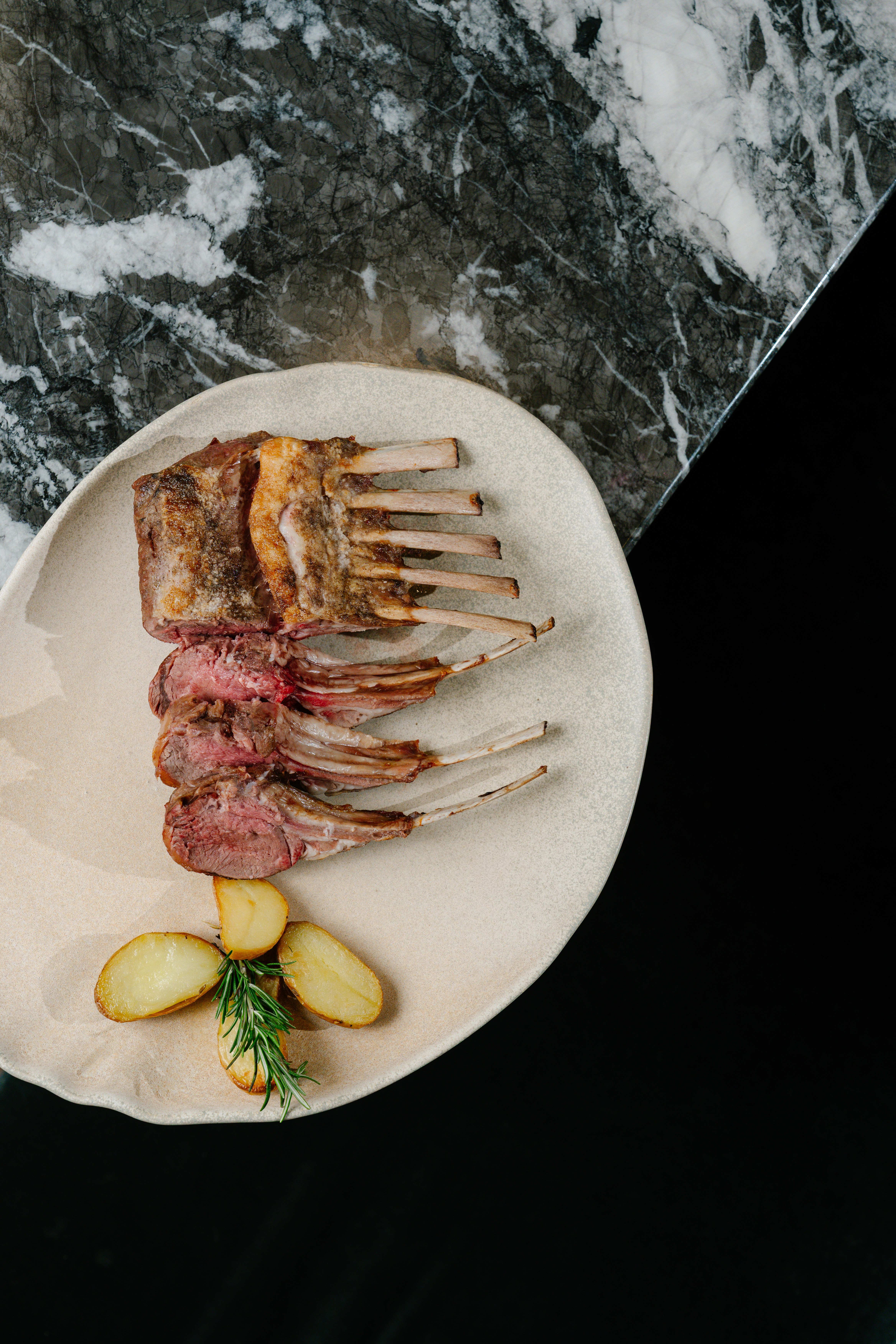 Sliced rack of lamb, medium-rare, with roasted potatoes and rosemary.
