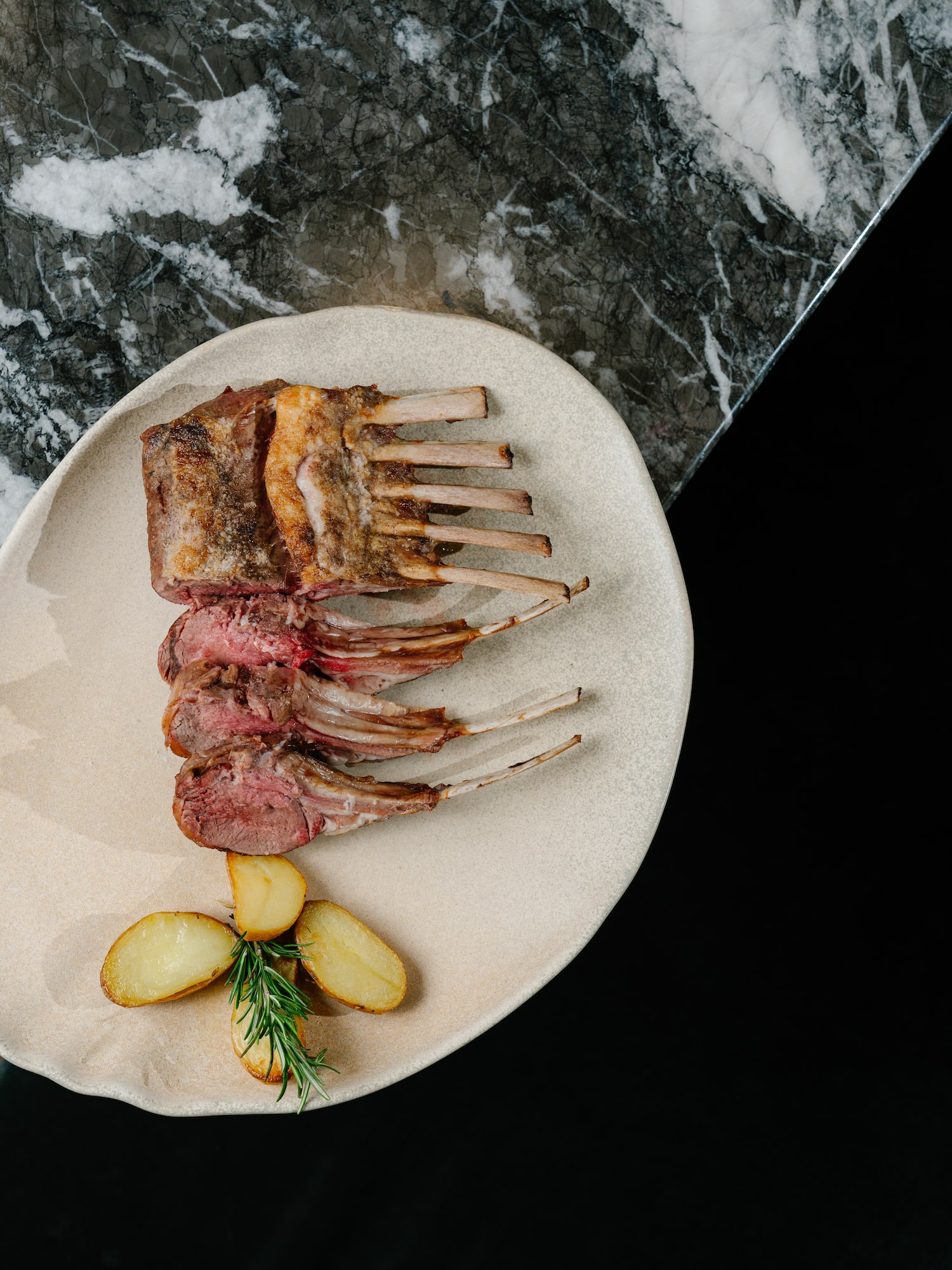 Sliced rack of lamb, medium-rare, with roasted potatoes and rosemary.