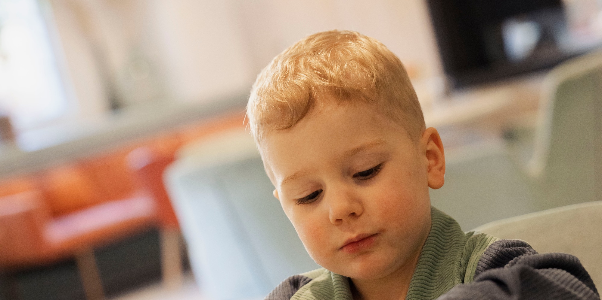 Young blonde boy playing with candies on a plate at a cafe table.