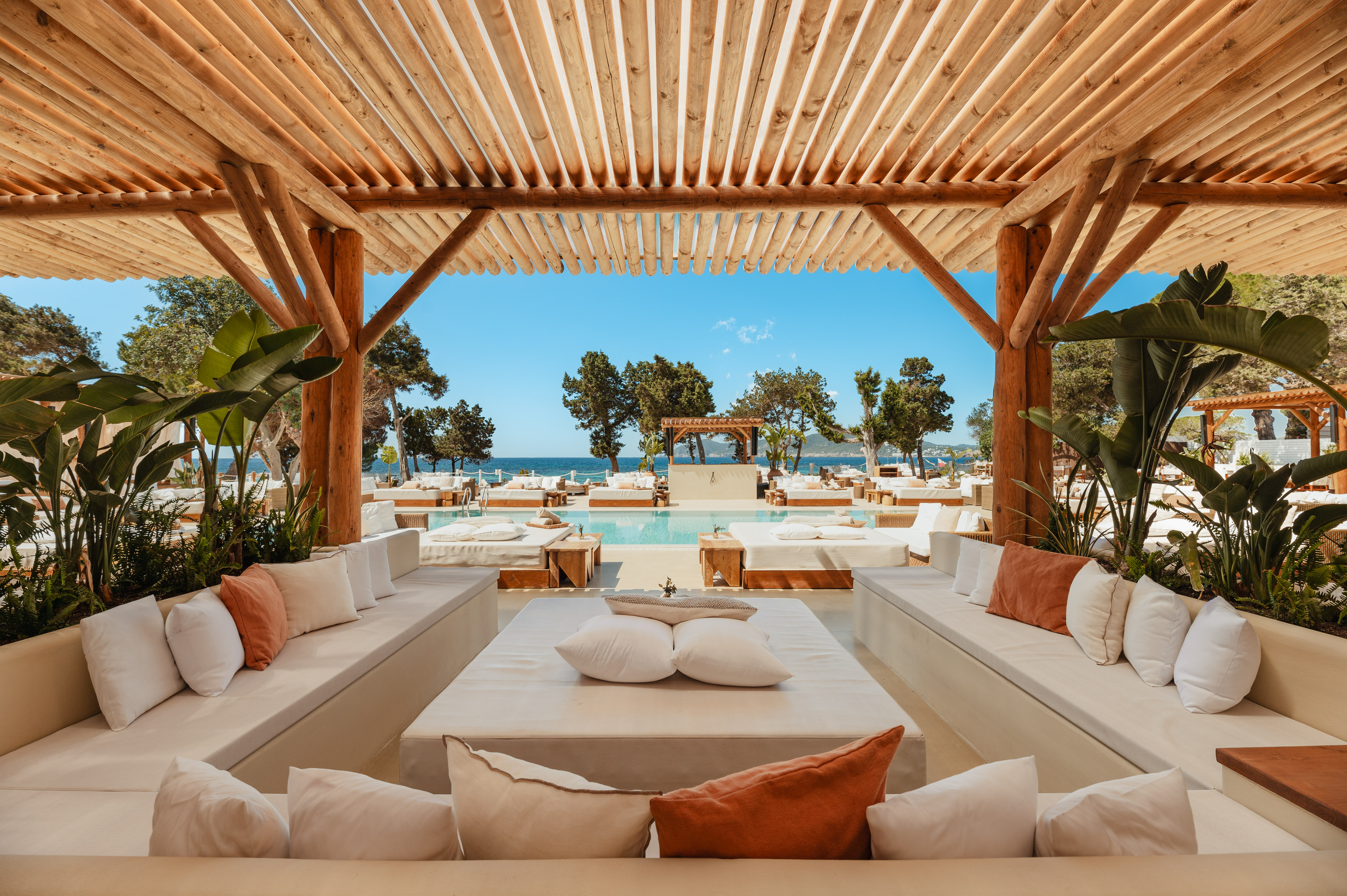 Luxury resort pool lounge under wooden pergola, daybeds, ocean view.