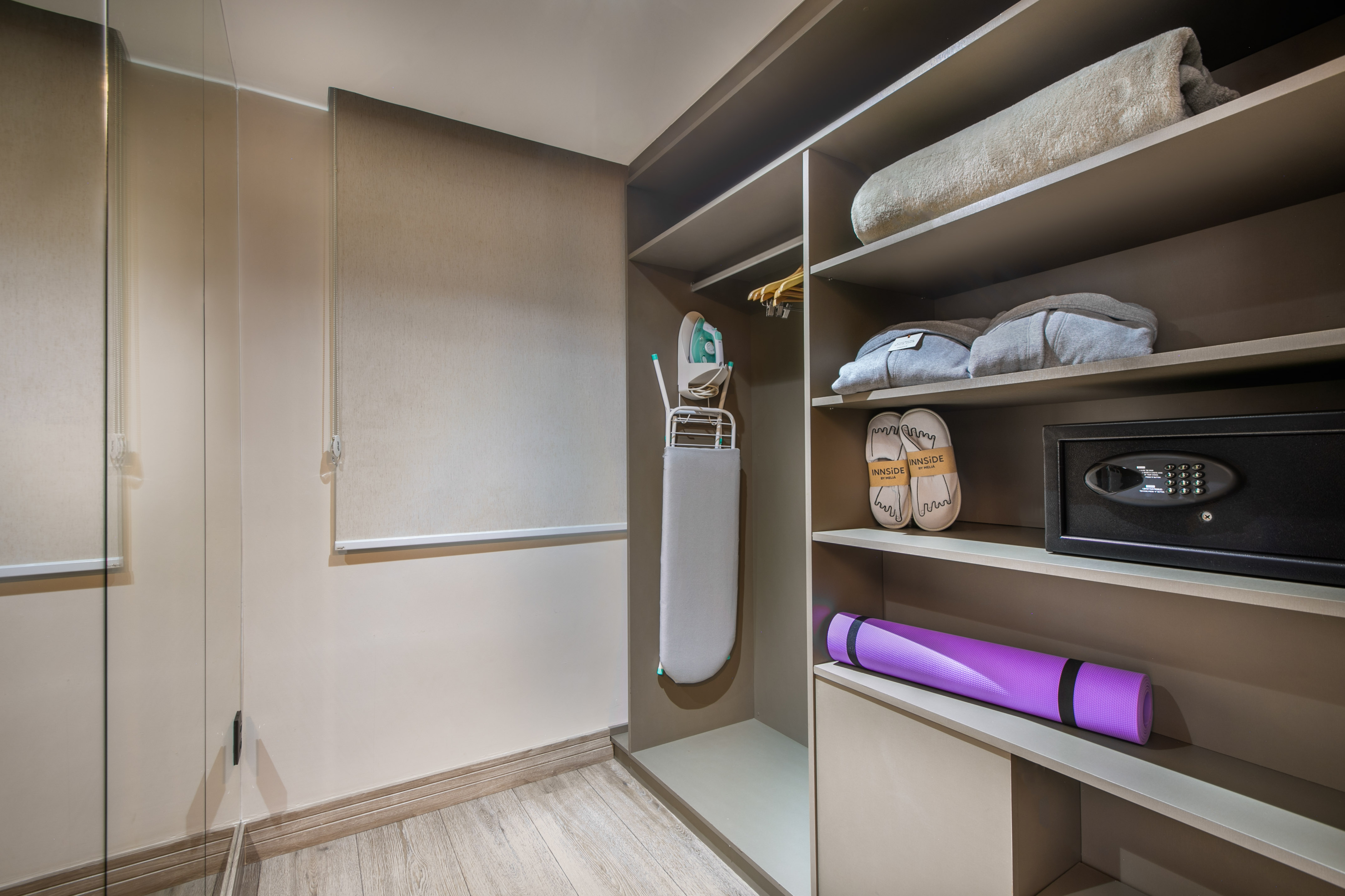 Modern hotel closet with ironing board, safe, slippers, yoga mat, and amenities.