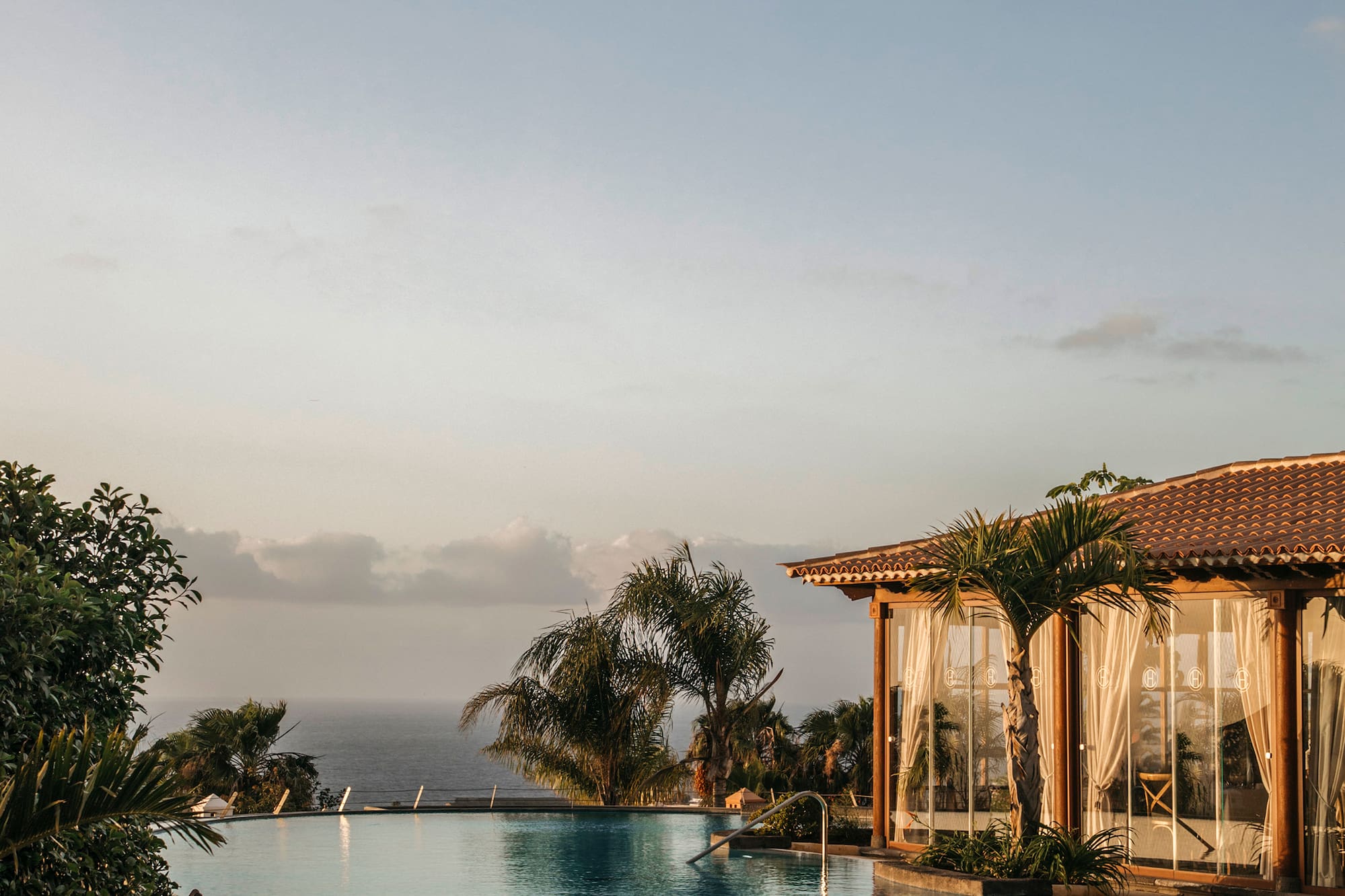 Oceanfront infinity pool with palm trees and resort building at sunset.