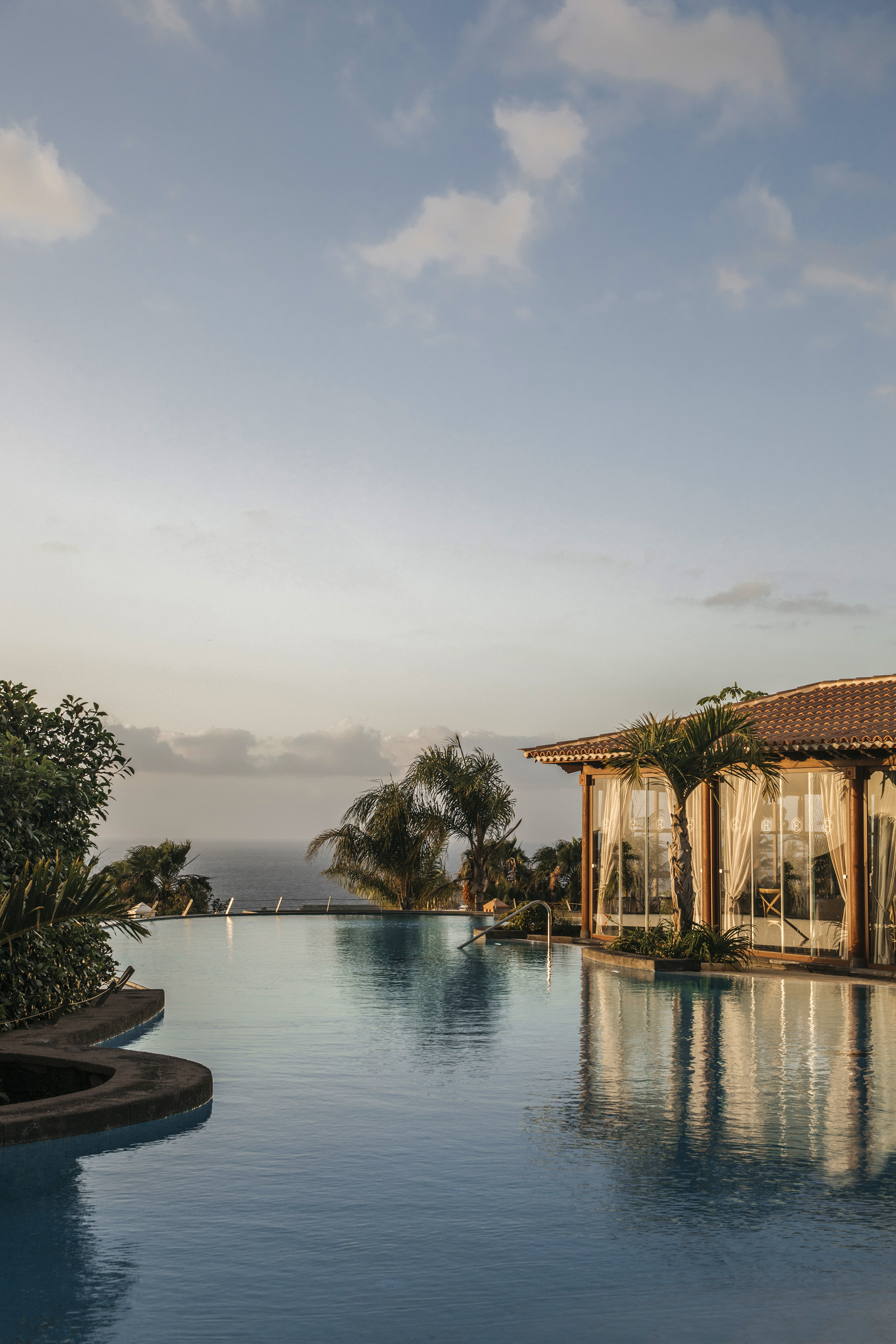 Oceanfront infinity pool with palm trees and resort building at sunset.