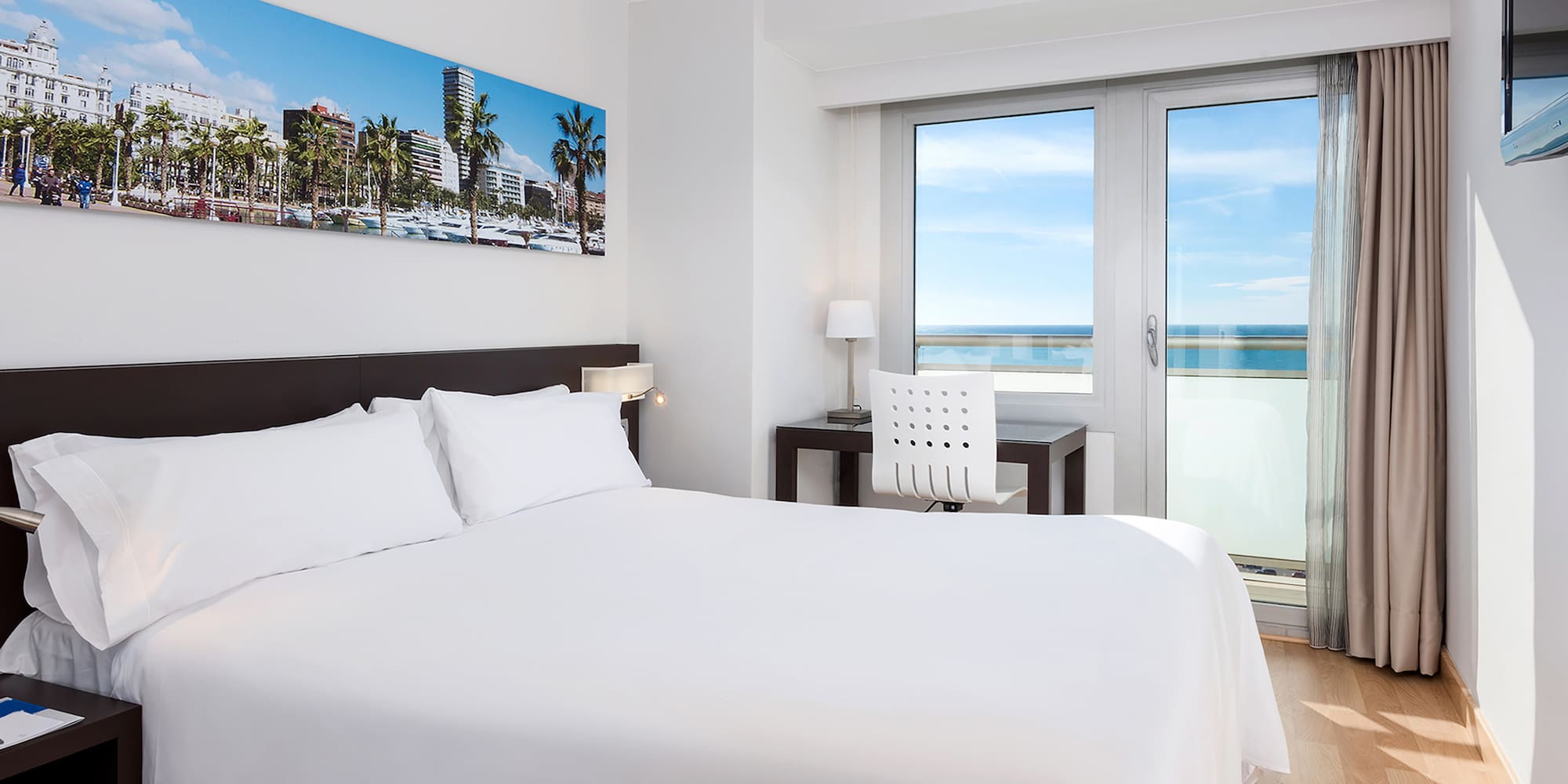 a bed with white sheets and a chair and a desk with a window