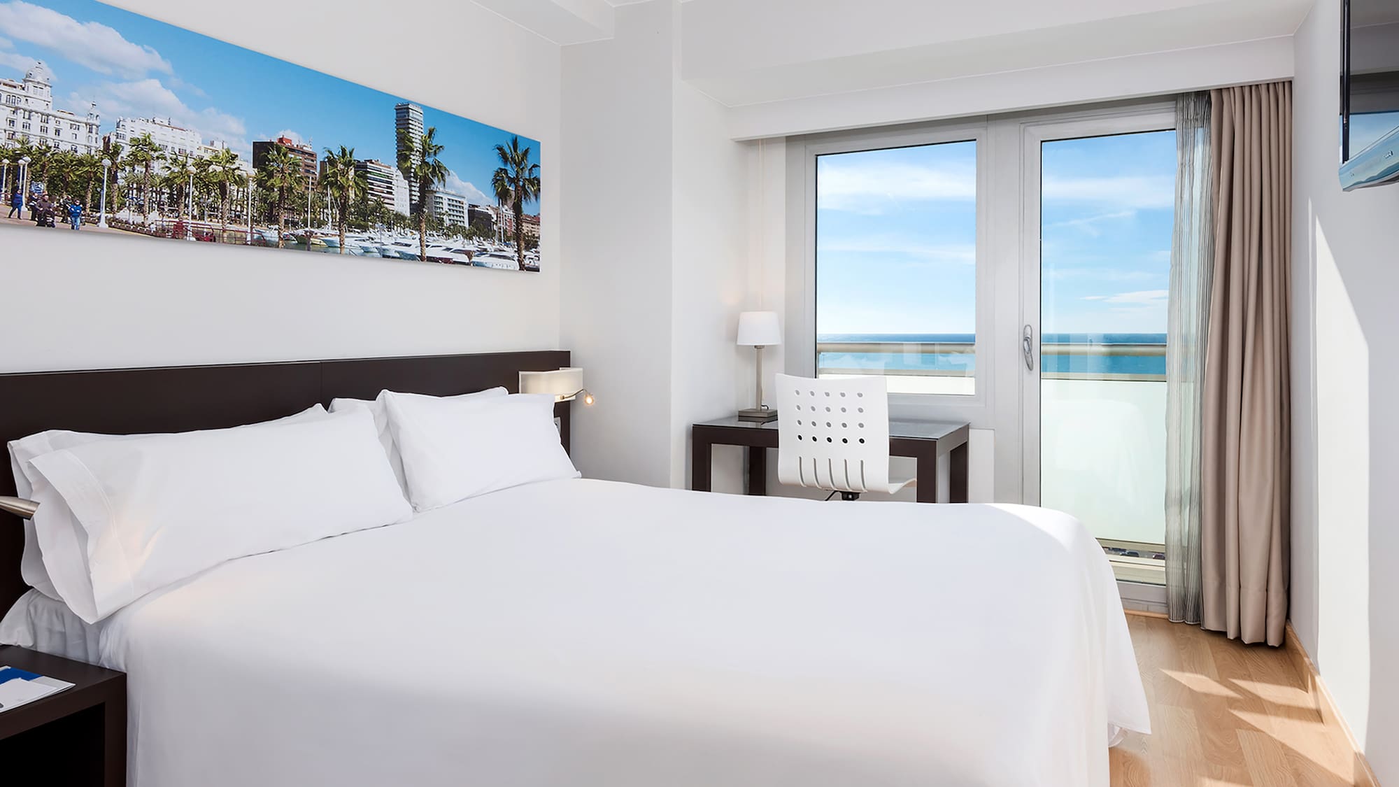 a bed with white sheets and a chair and a desk with a window
