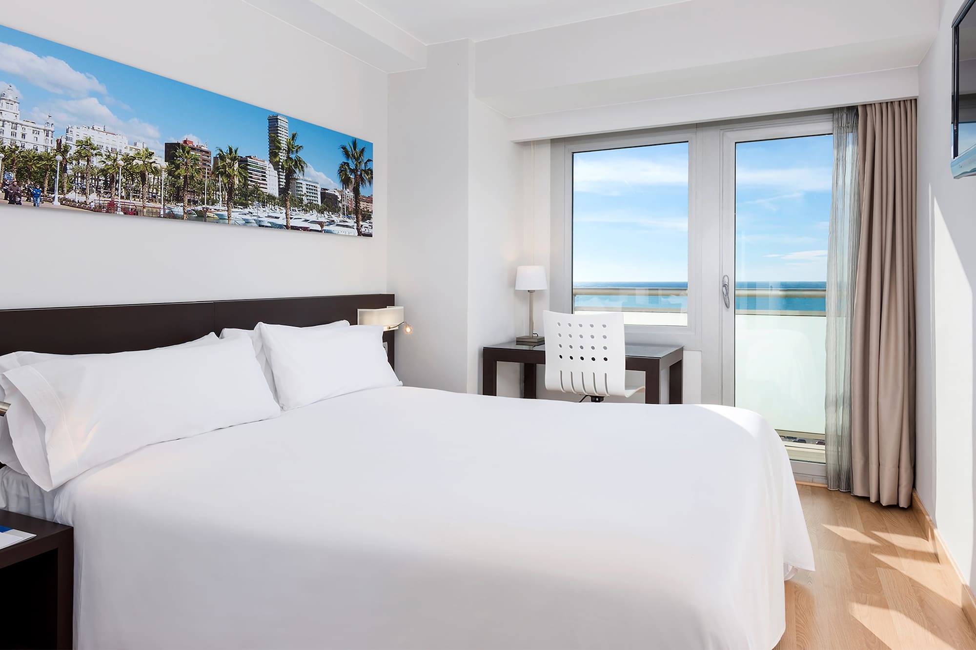 a bed with white sheets and a chair and a desk with a window