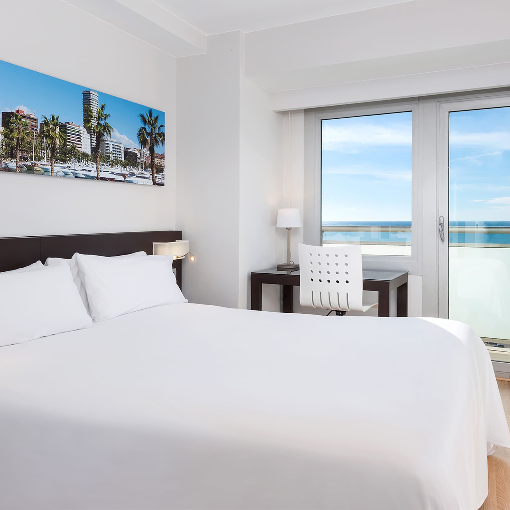 a bed with white sheets and a chair and a desk with a window