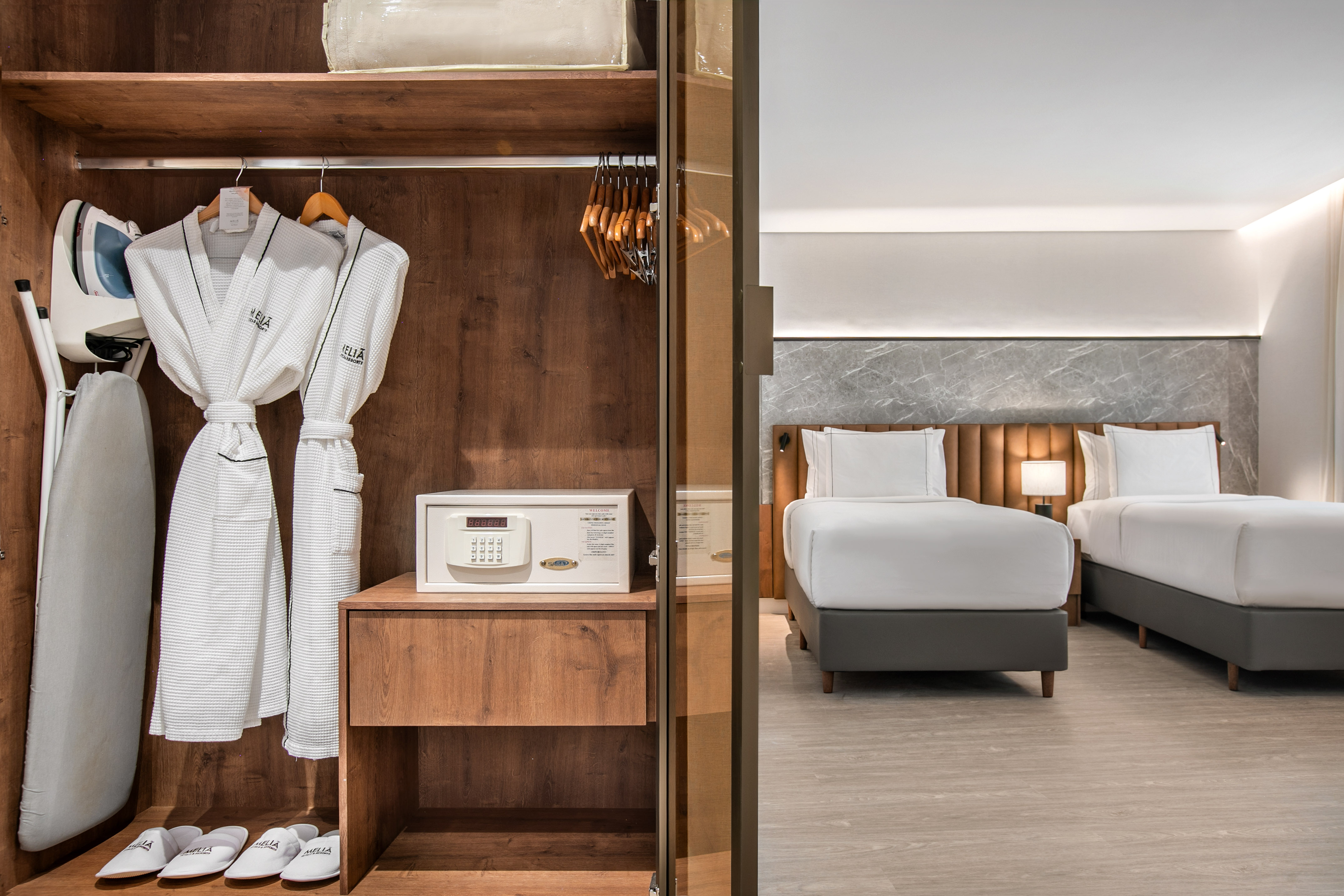 Hotel room: open closet with bathrobes, safe, iron, and two beds.