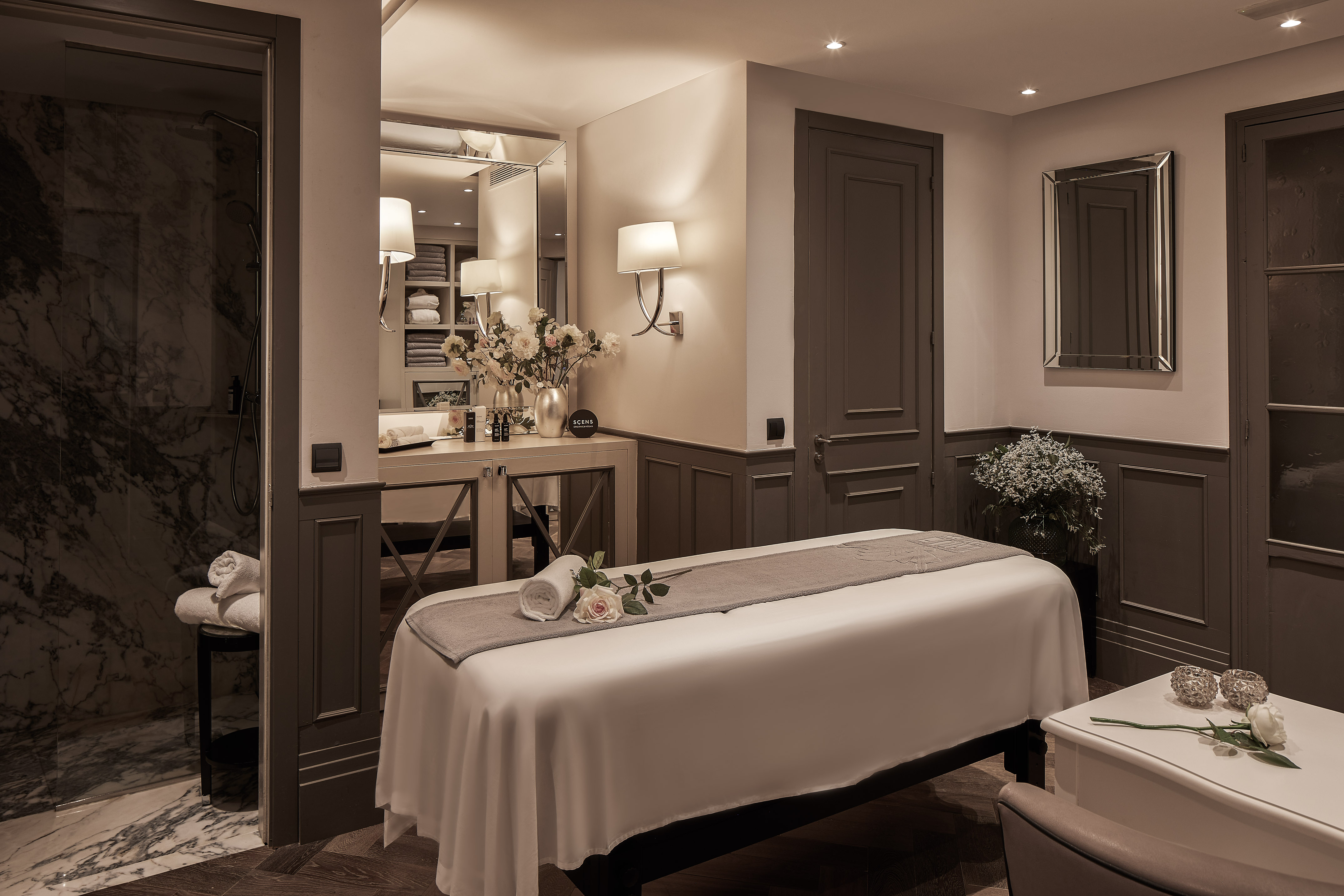 Tranquil spa treatment room with massage bed, white towels, and marble shower.