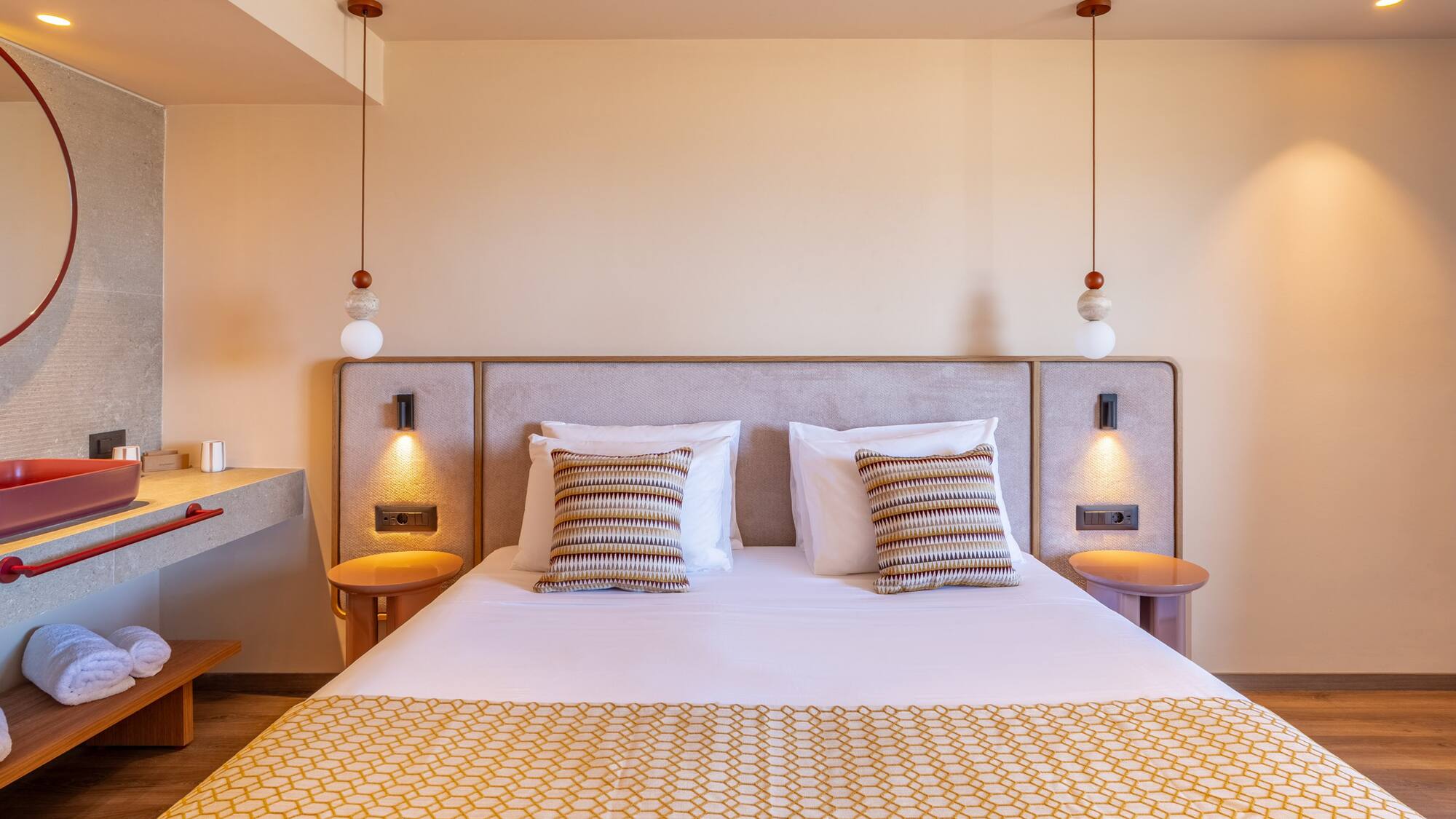 Modern hotel bedroom with patterned bed, pendant lights, and modern red-basin ensuite.