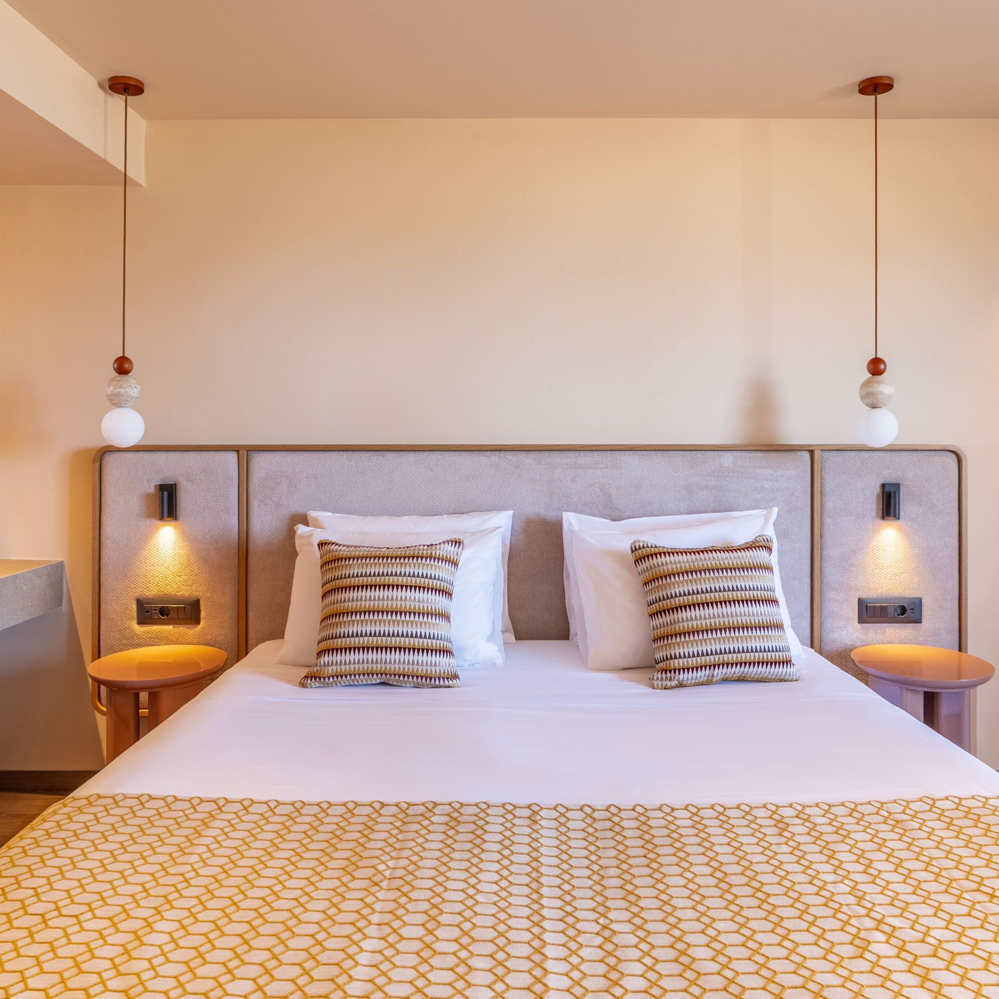 Modern hotel bedroom with patterned bed, pendant lights, and modern red-basin ensuite.