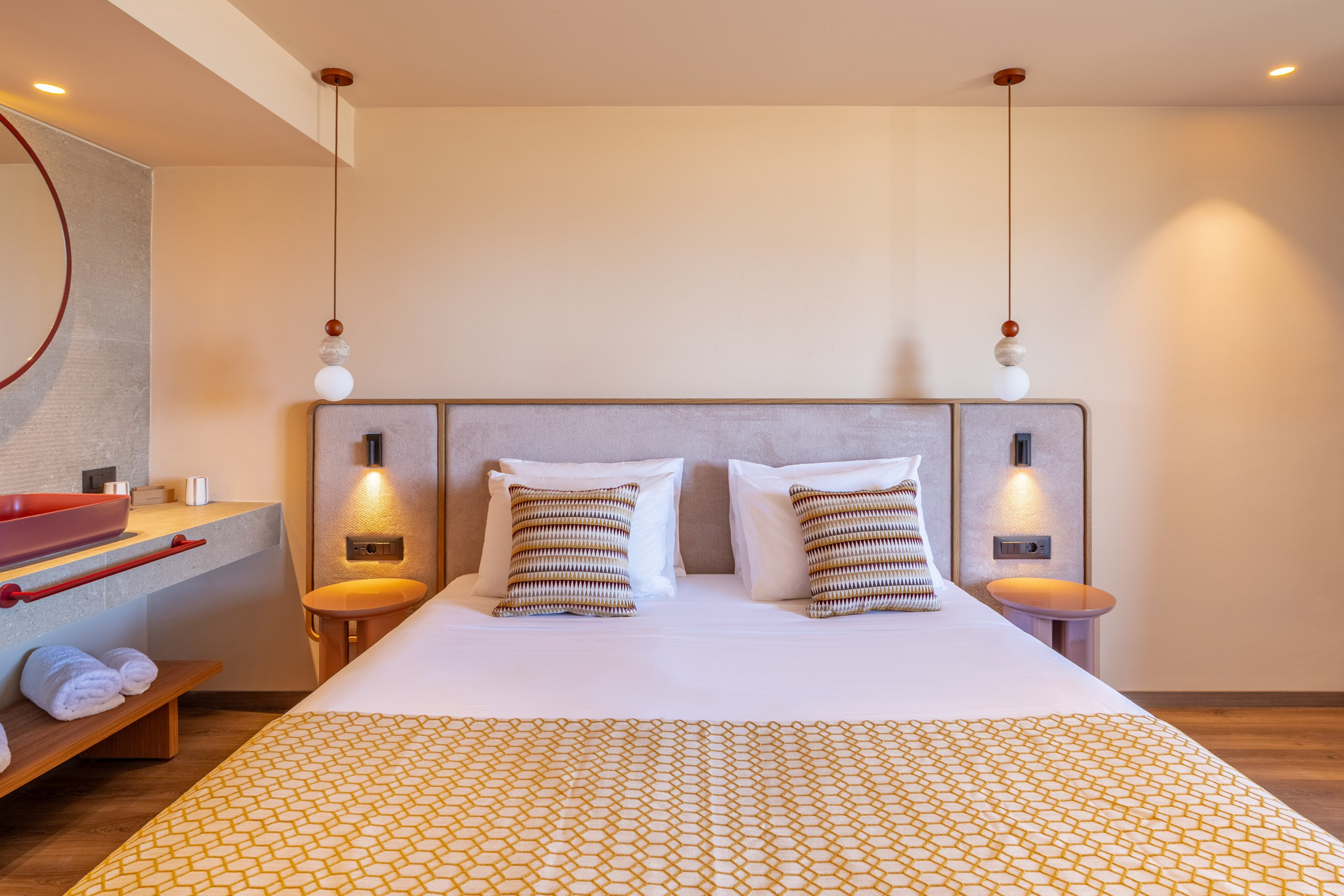 Modern hotel bedroom with patterned bed, pendant lights, and modern red-basin ensuite.