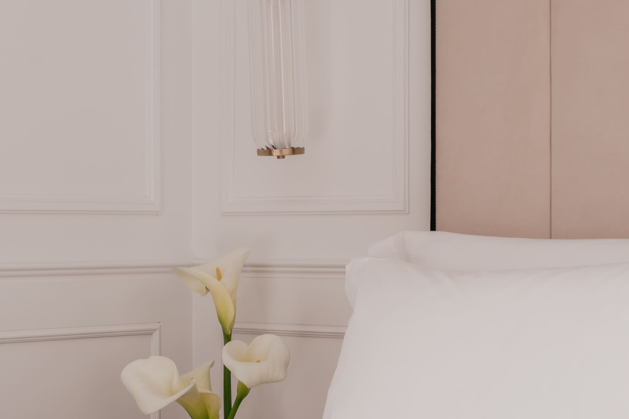 Elegant bedroom with brass wall sconce, white calla lilies, and crisp bedding.