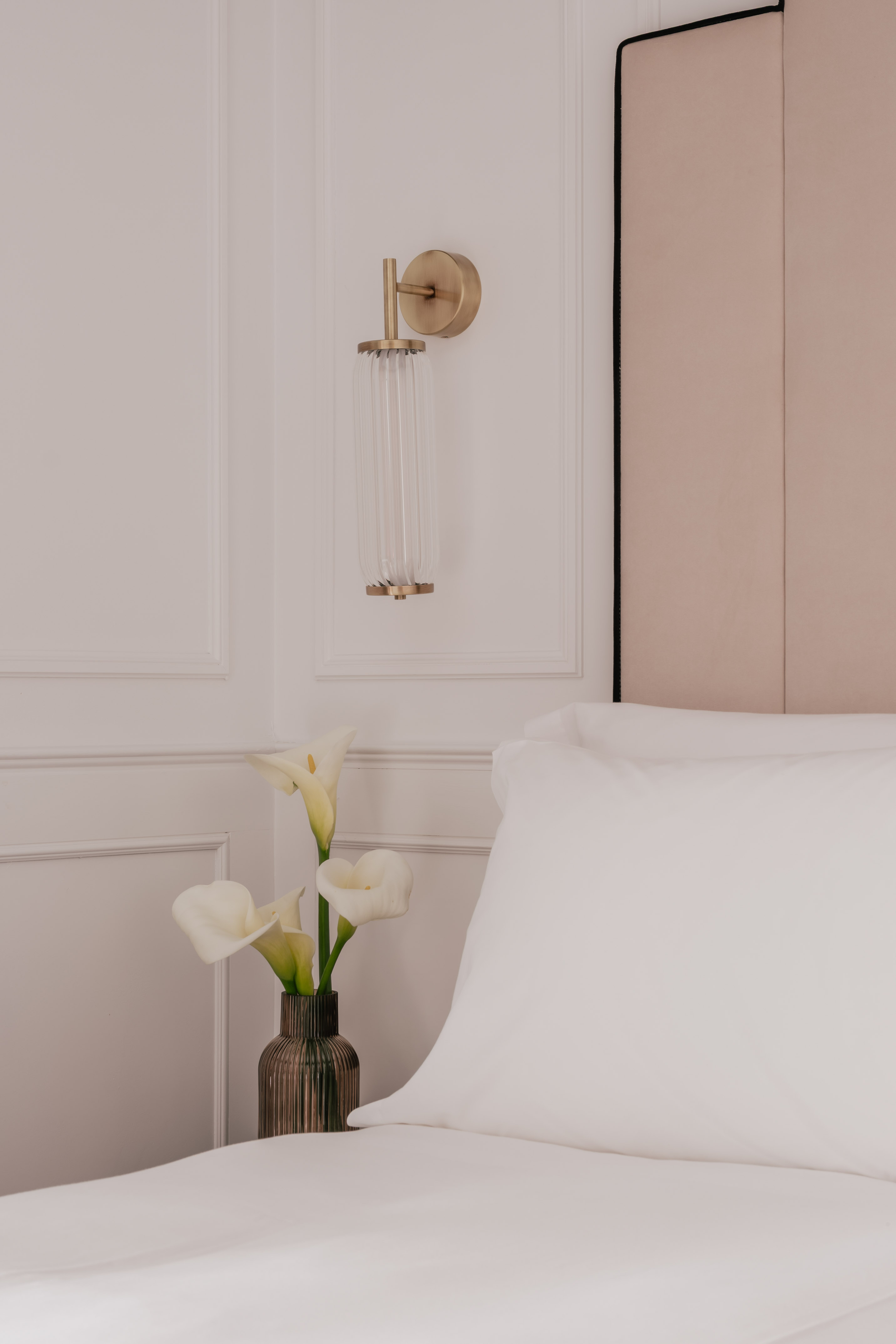 Elegant bedroom with brass wall sconce, white calla lilies, and crisp bedding.