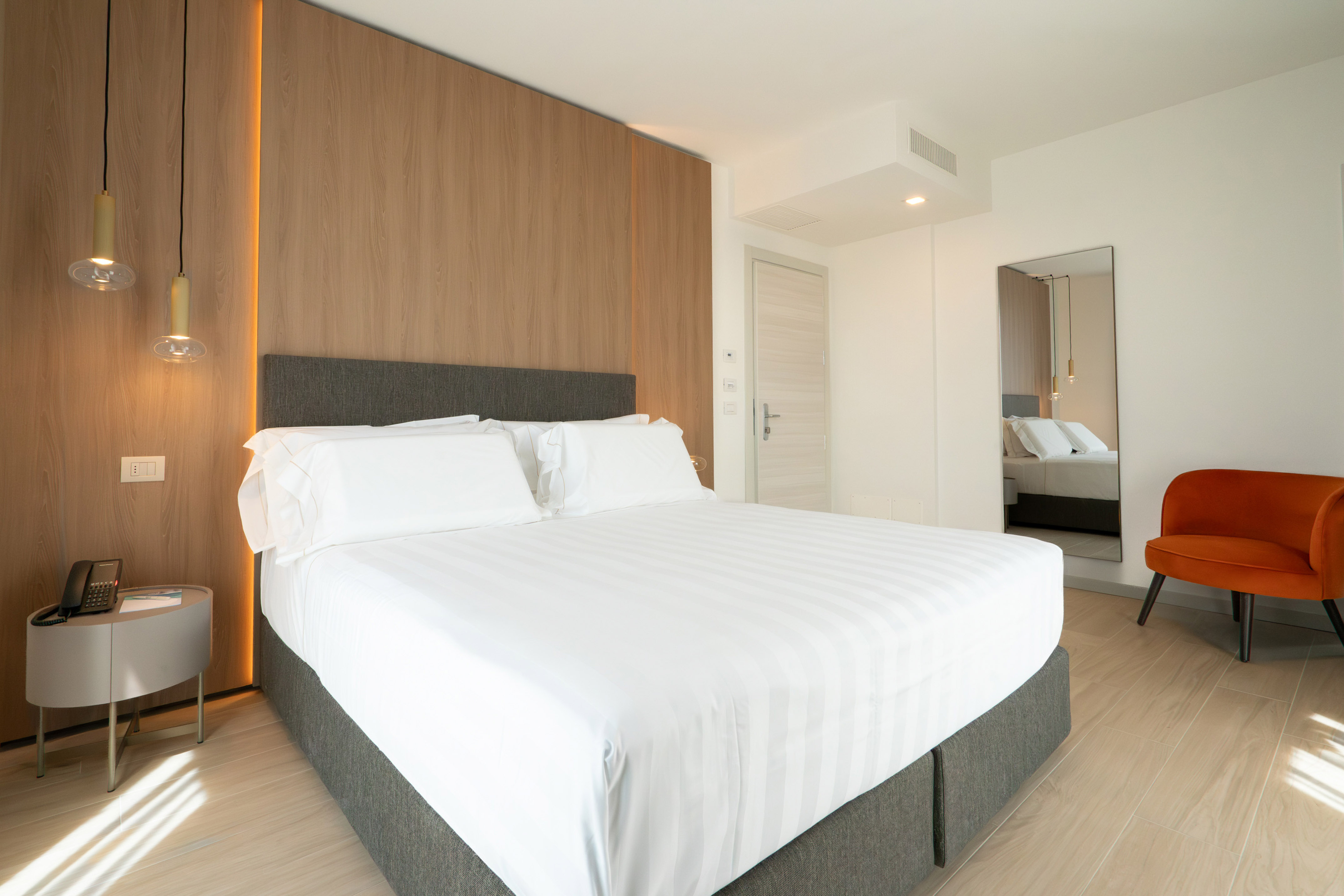 Modern hotel bedroom with king bed, wooden headboard, and orange accent chair.
