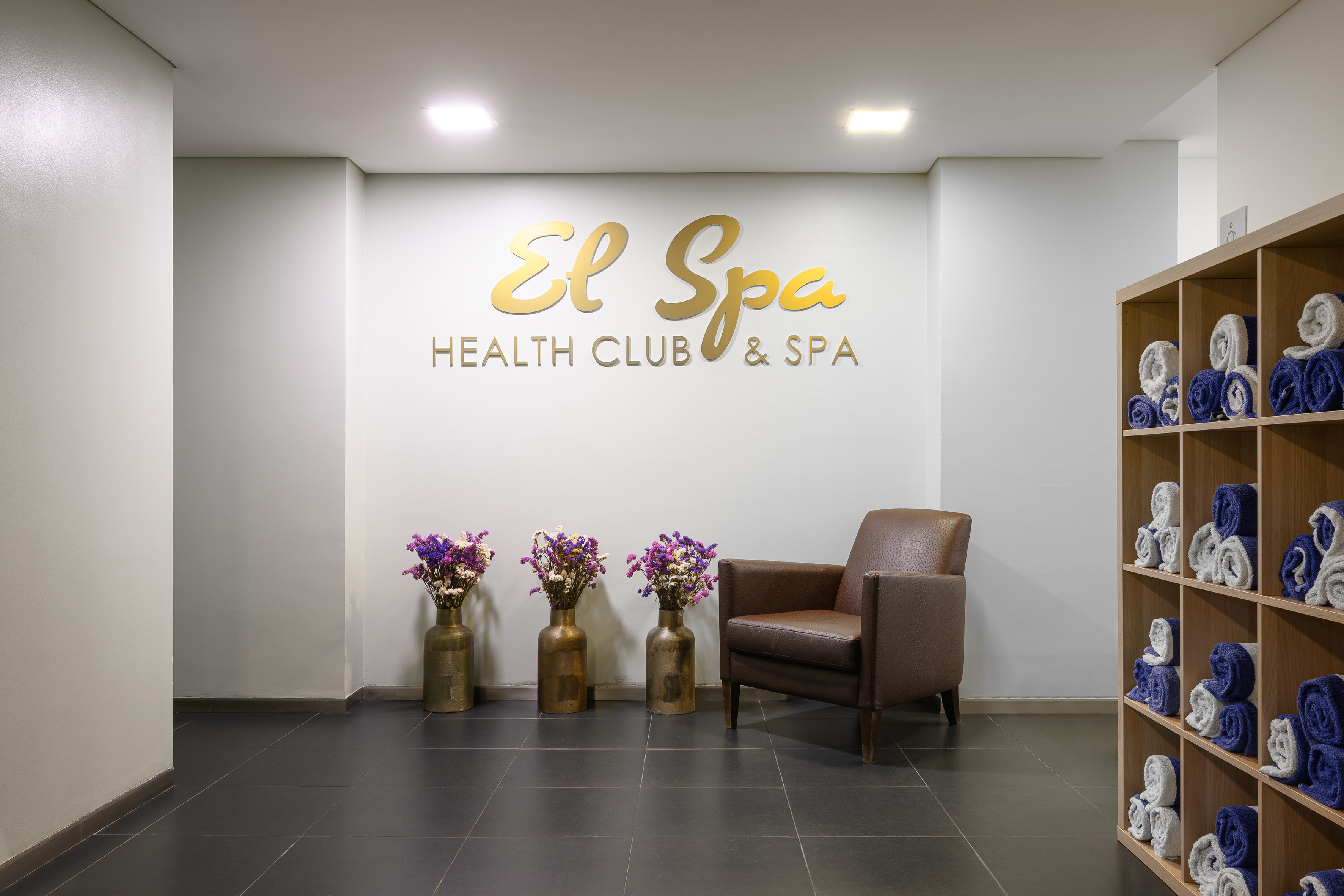 El Spa Health Club & Spa gold sign, brown armchair, floral decor, rolled towels.