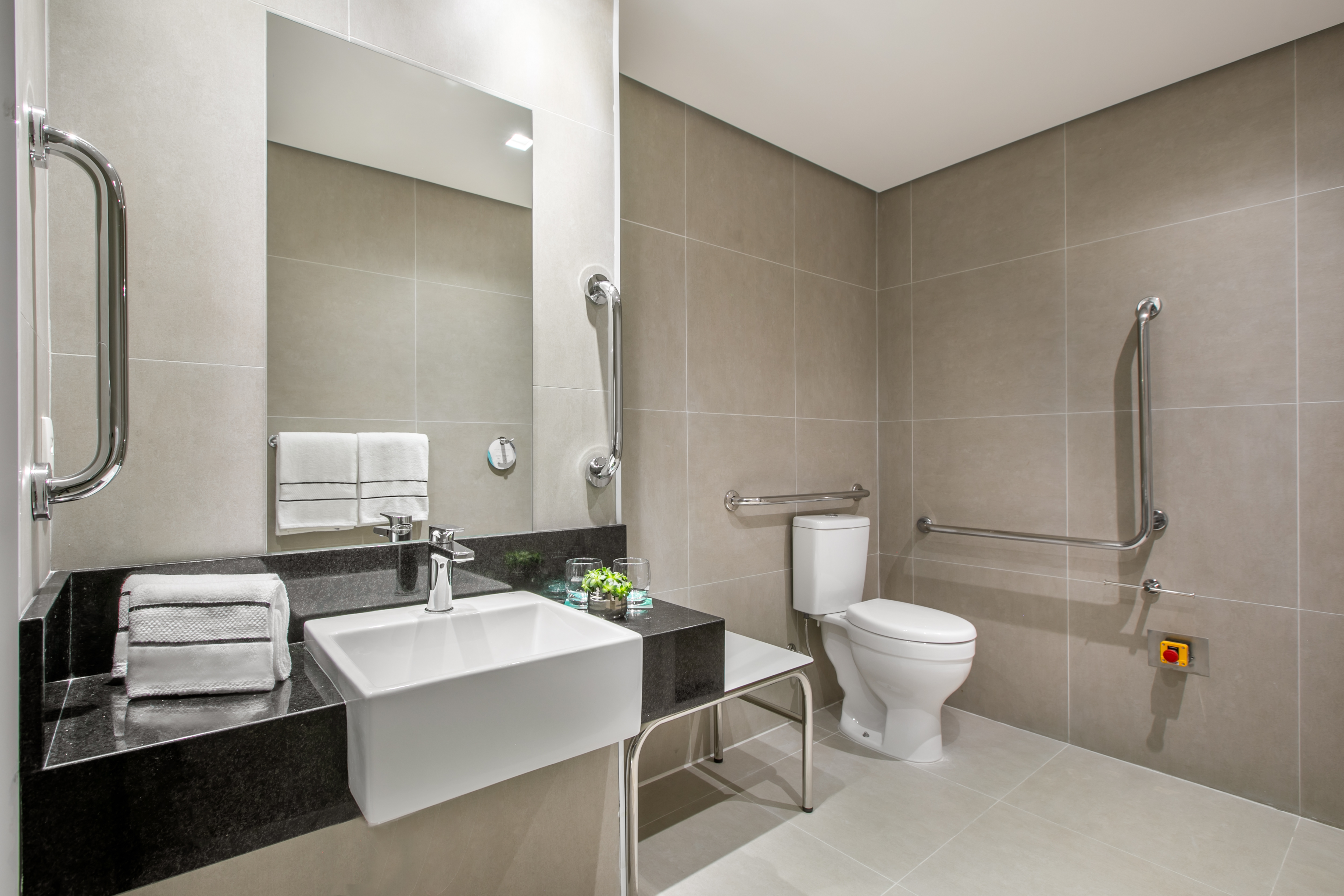 ADA bathroom with grab bars, gray tiles, modern sink, and toilet.