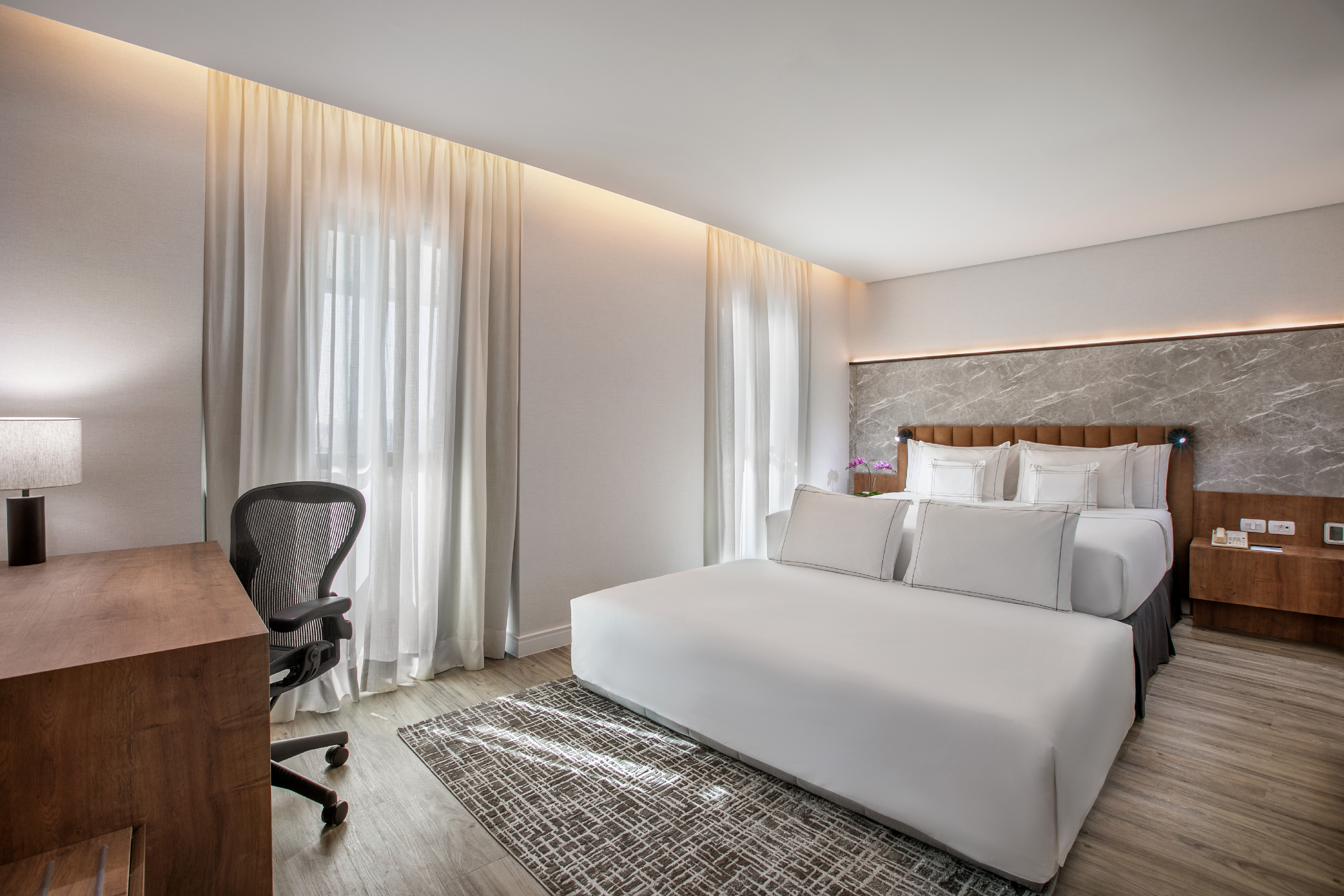 Modern hotel room with king bed, desk, office chair, and marble accent wall.