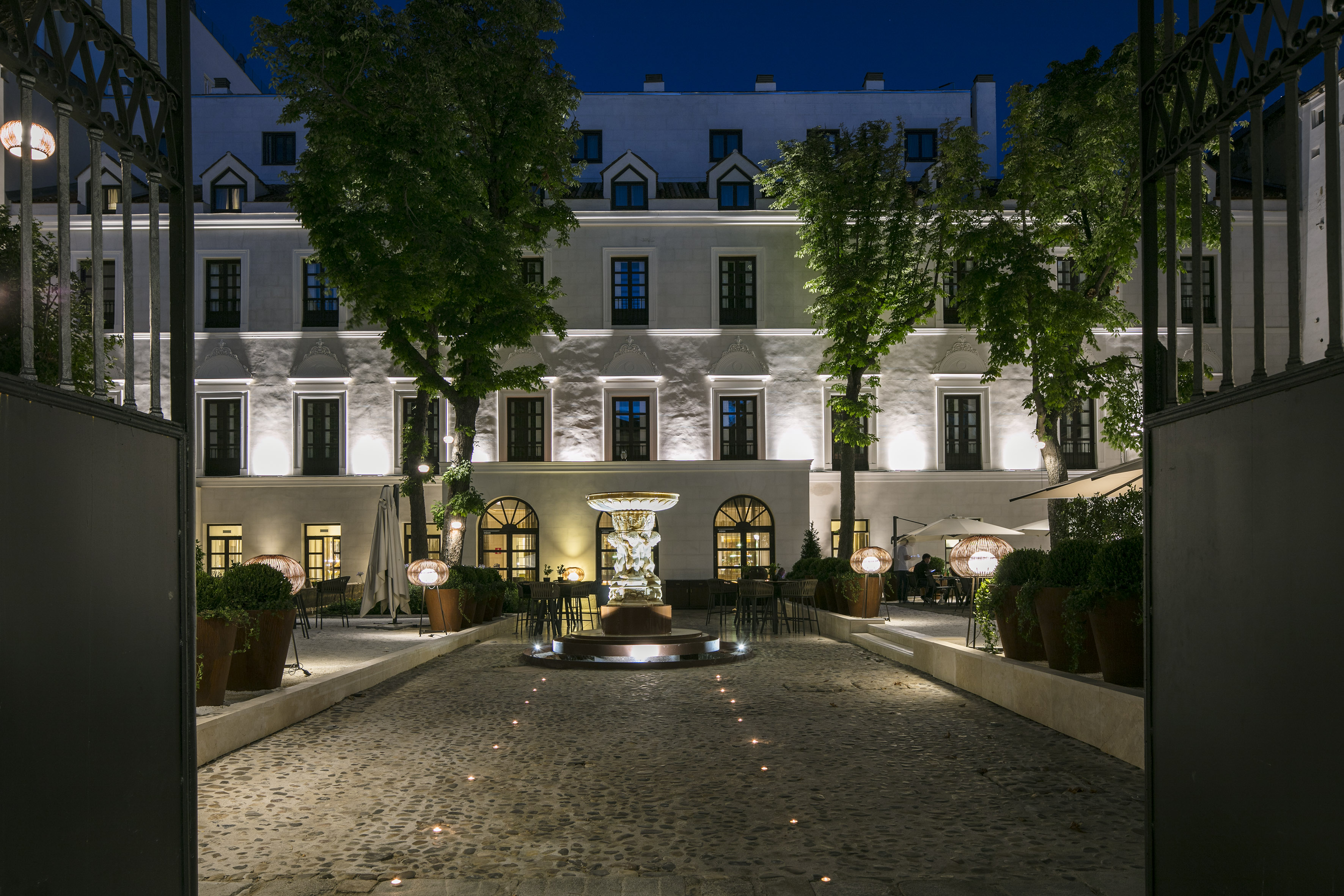 Hotel courtyard at night, illuminated fountain, cobblestone path, outdoor dining areas.