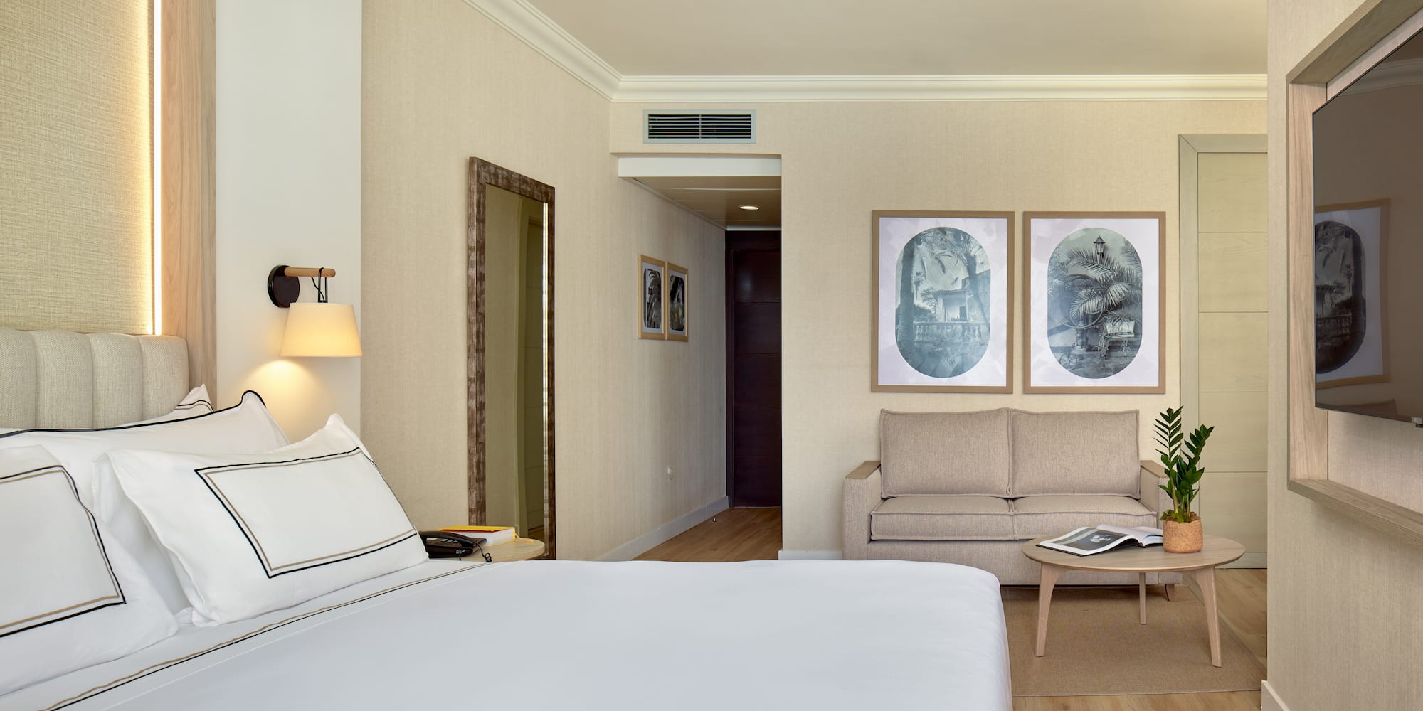 Neutral hotel suite with bed, sitting area, modern decor, and hardwood floor.