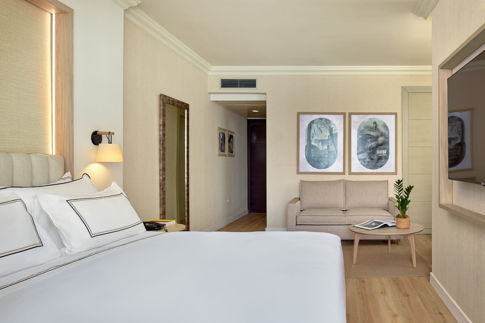 Stylish hotel suite with comfortable bed, sofa, wall art, and warm lighting.