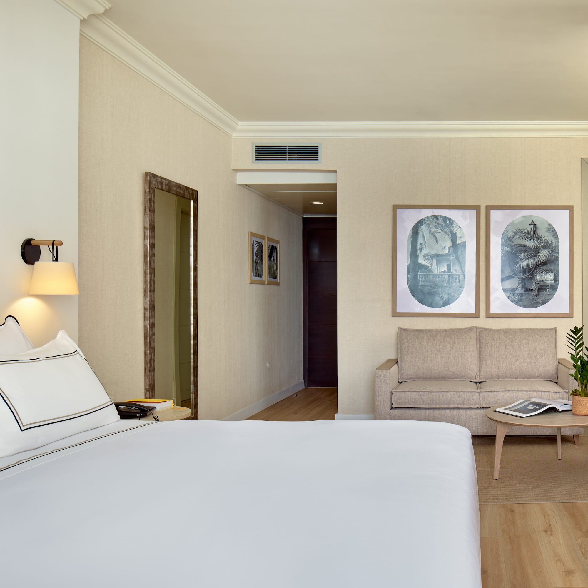 Stylish hotel suite with comfortable bed, sofa, wall art, and warm lighting.