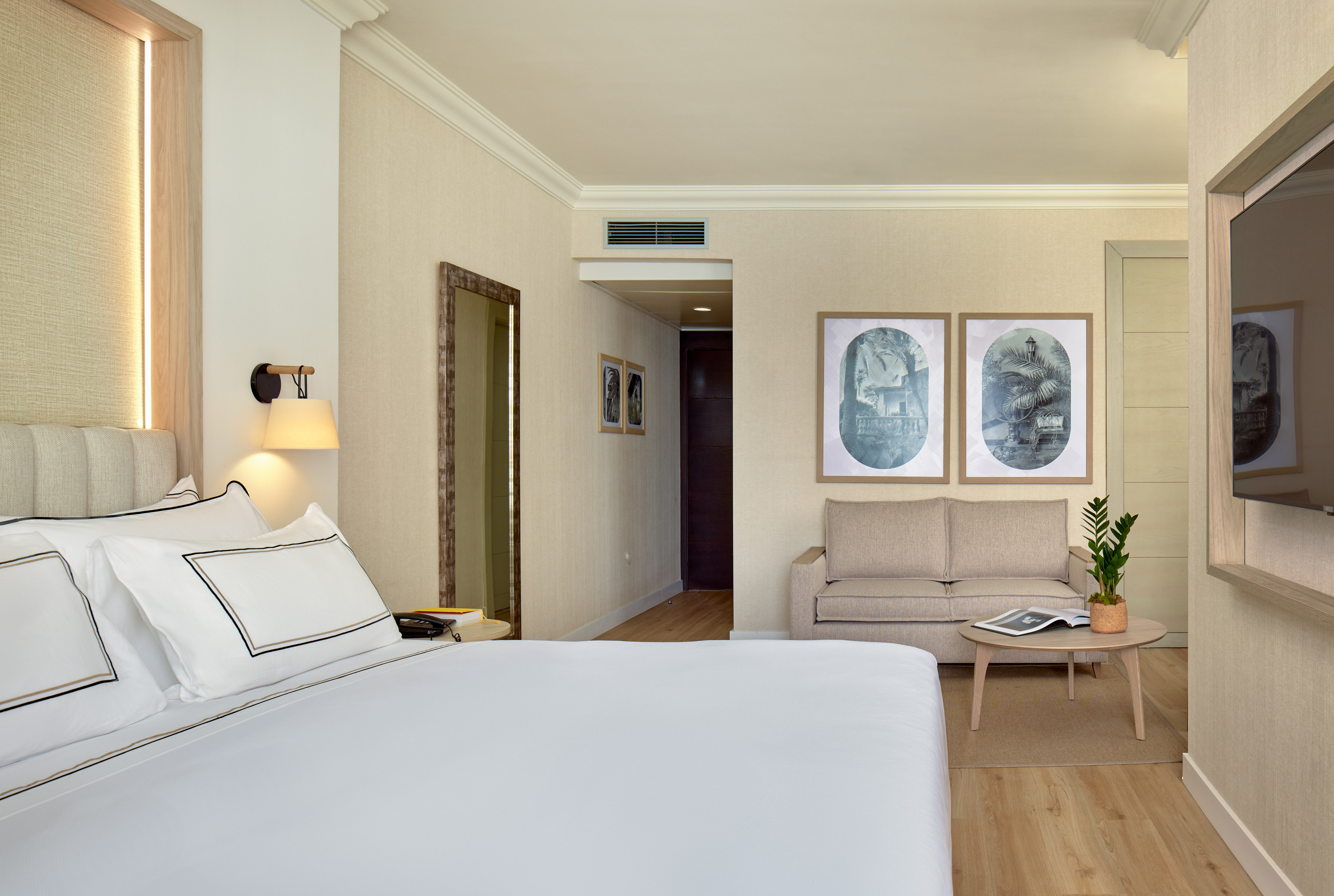 Stylish hotel suite with comfortable bed, sofa, wall art, and warm lighting.