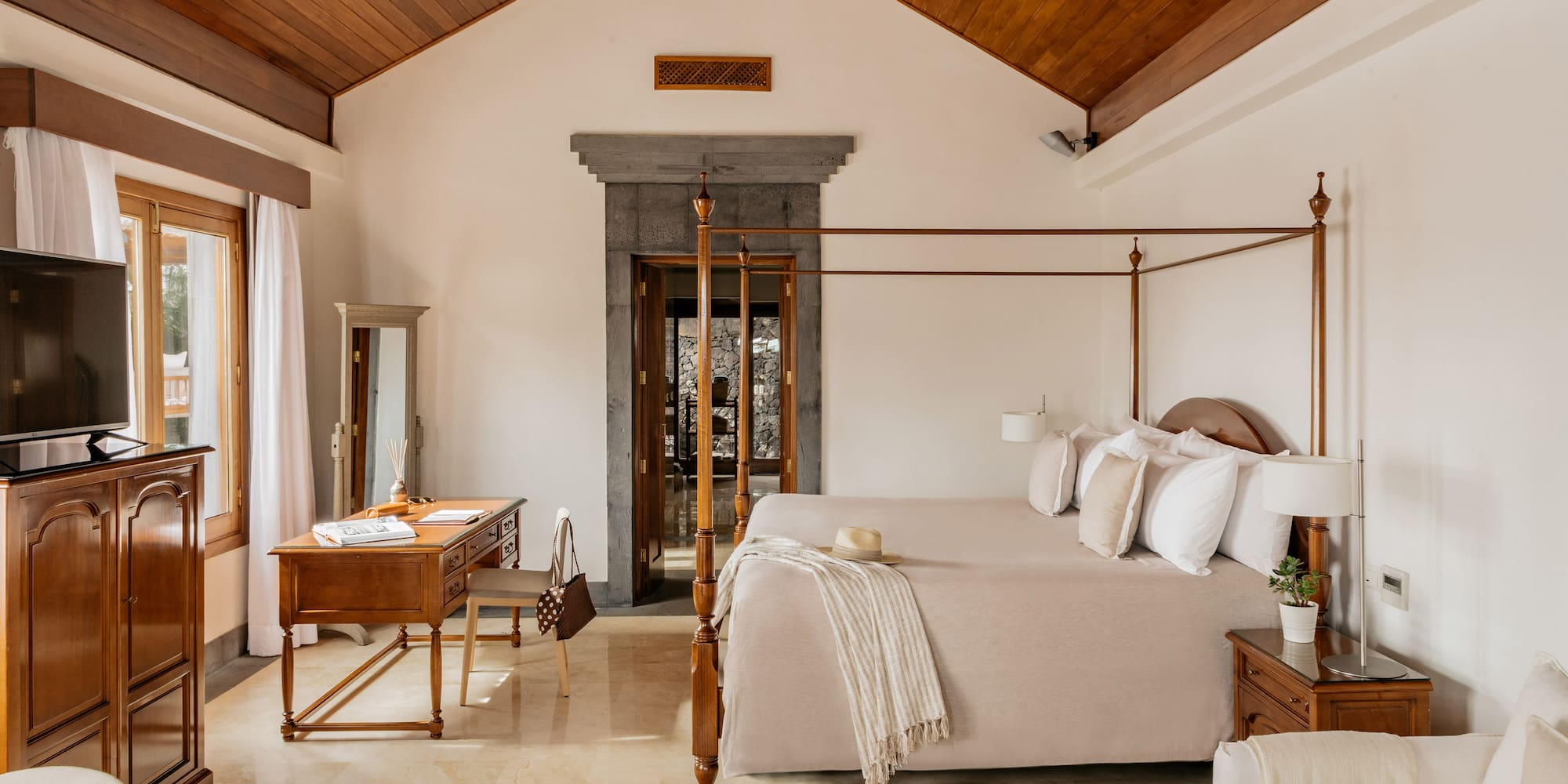 Luxury hotel bedroom with four-poster bed, vaulted wood ceiling, and stone doorway.
