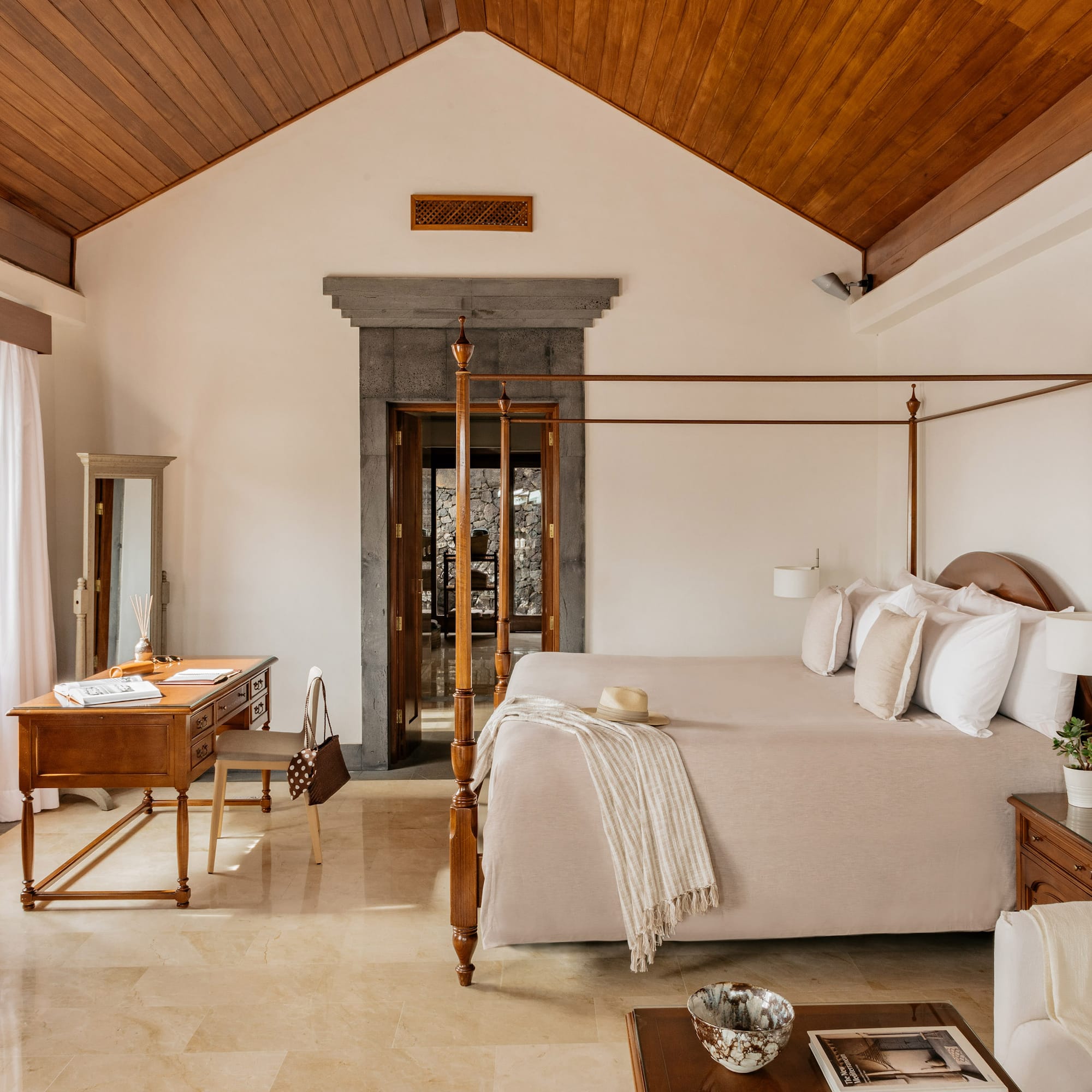 Luxury hotel bedroom with four-poster bed, vaulted wood ceiling, and stone doorway.