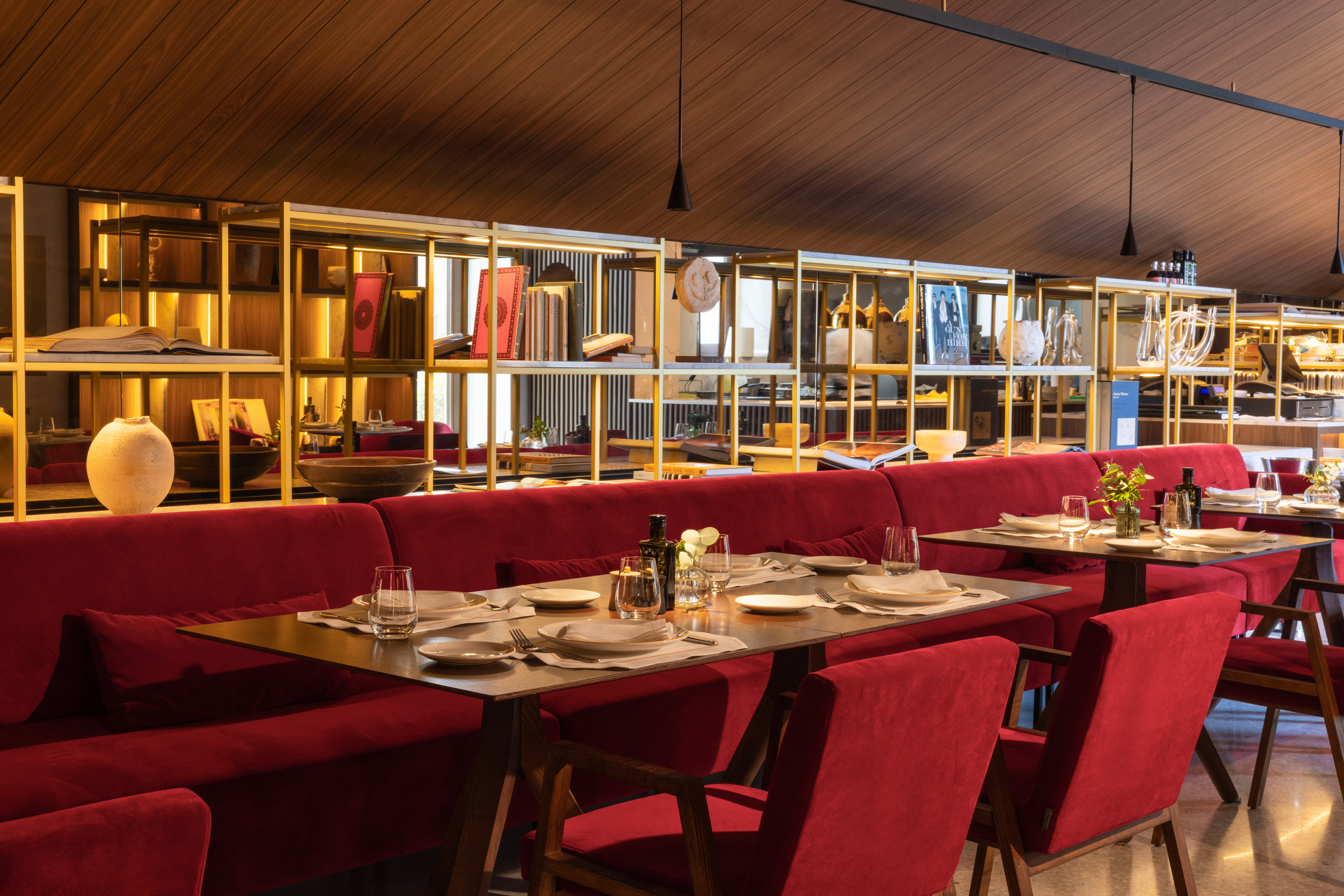 Restaurant dining area with red velvet seating, set tables, and gold shelving.