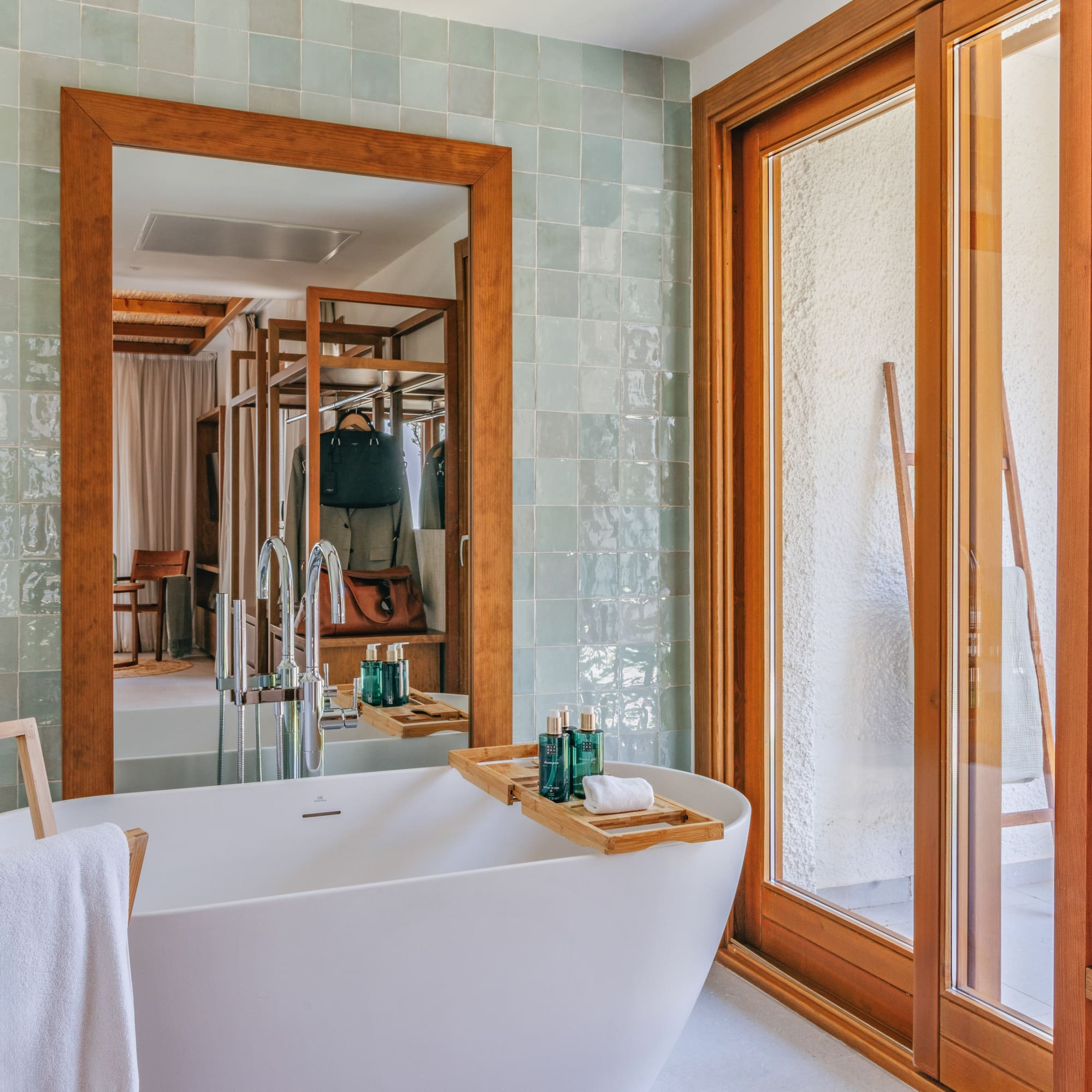 Modern bathroom with white tub, green tiles, wooden mirror, and sliding door.
