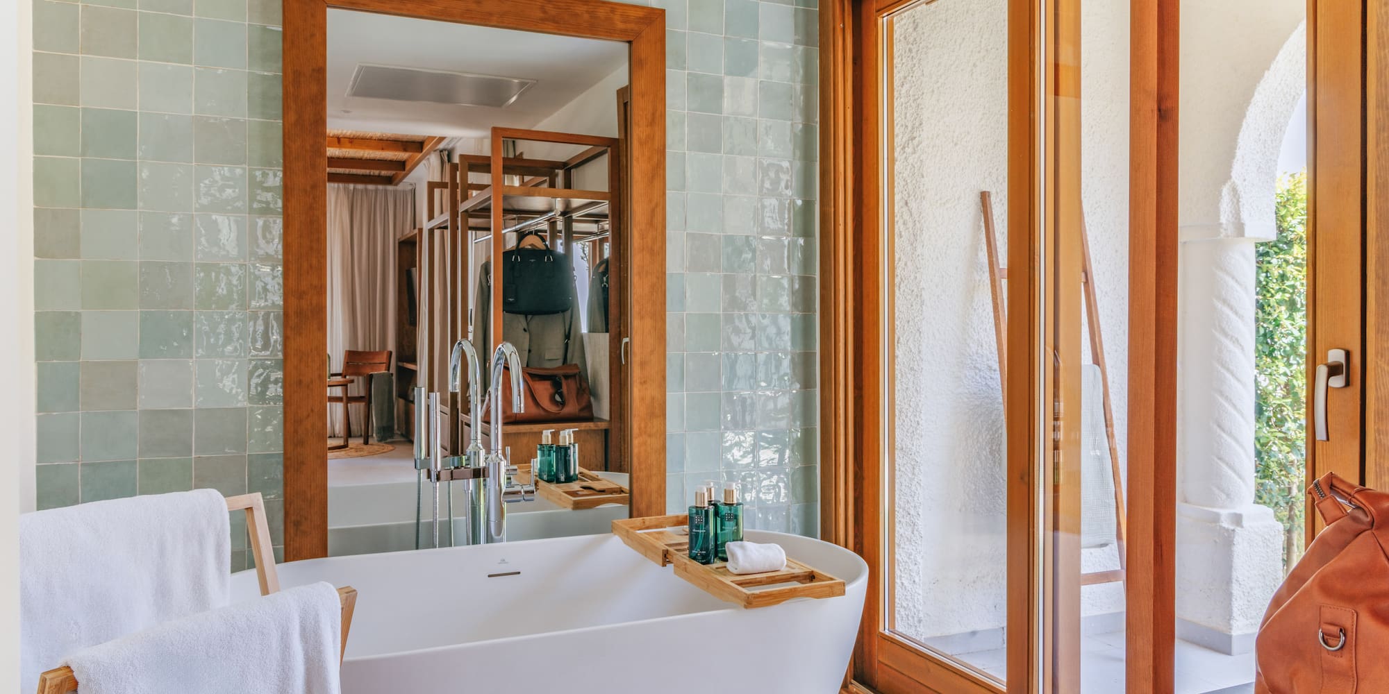 Modern bathroom with white tub, green tiles, wooden mirror, and sliding door.