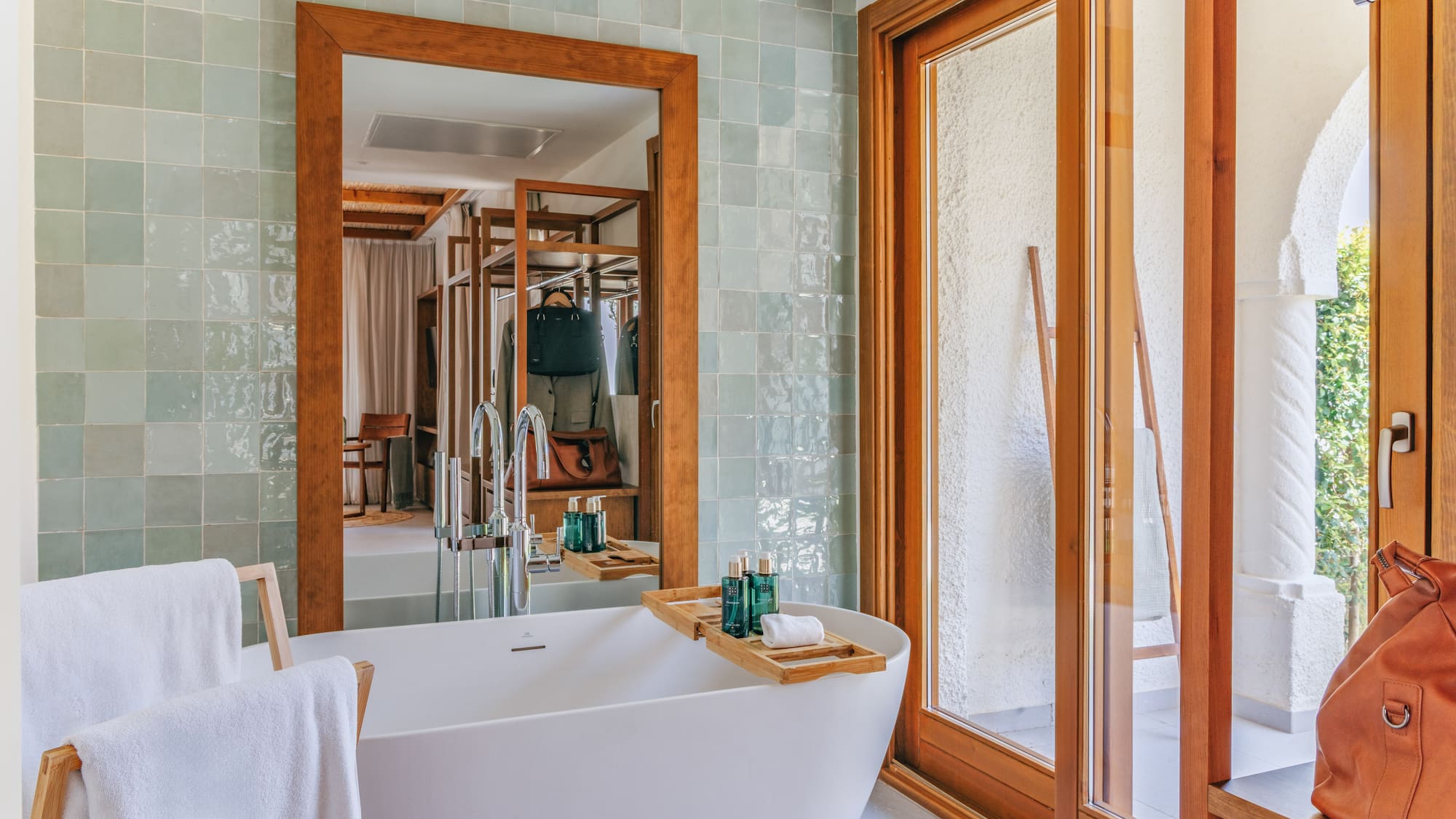 Modern bathroom with white tub, green tiles, wooden mirror, and sliding door.
