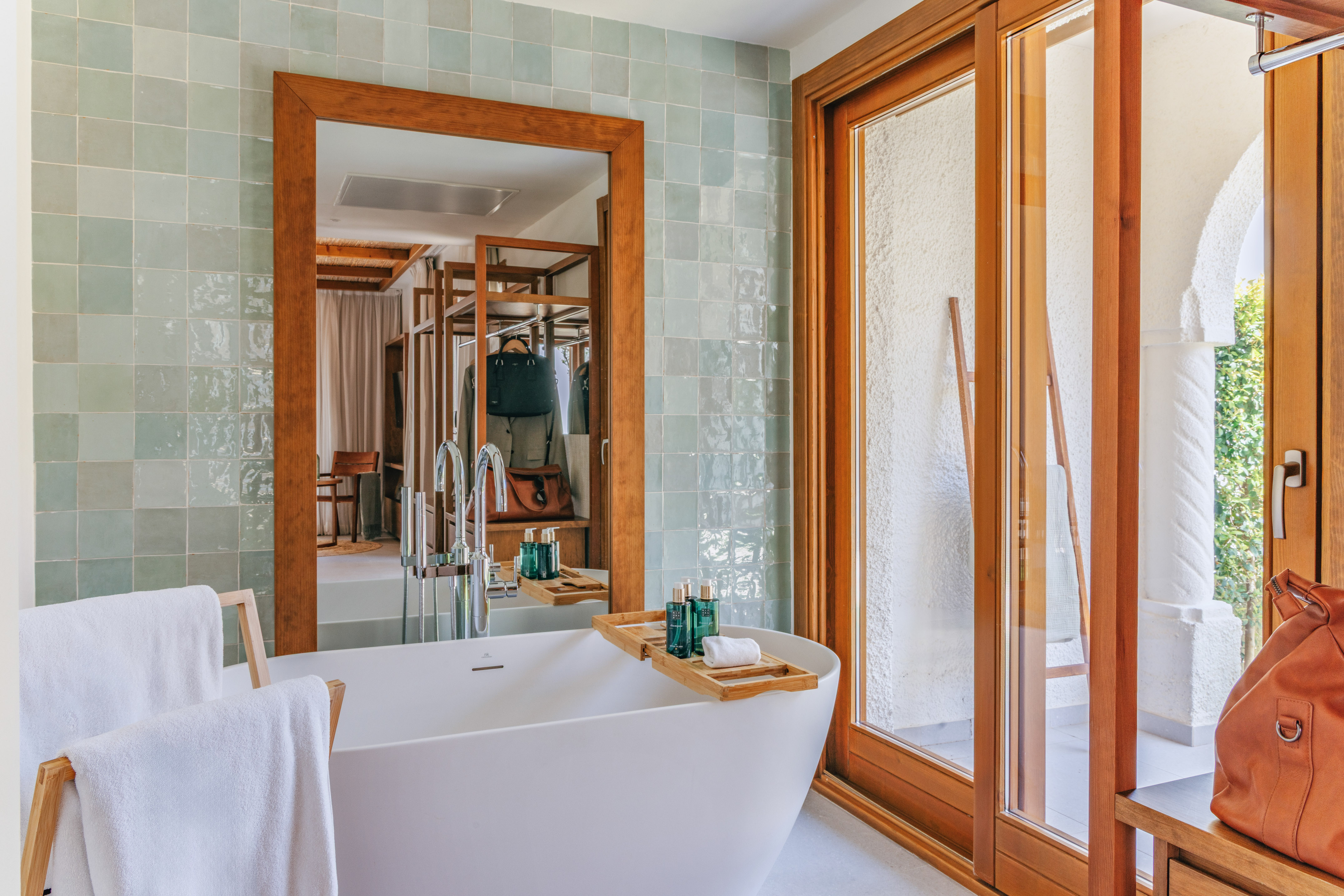 Modern bathroom with white tub, green tiles, wooden mirror, and sliding door.