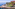 Red hotel on rocky coast with green trees and clear blue ocean.