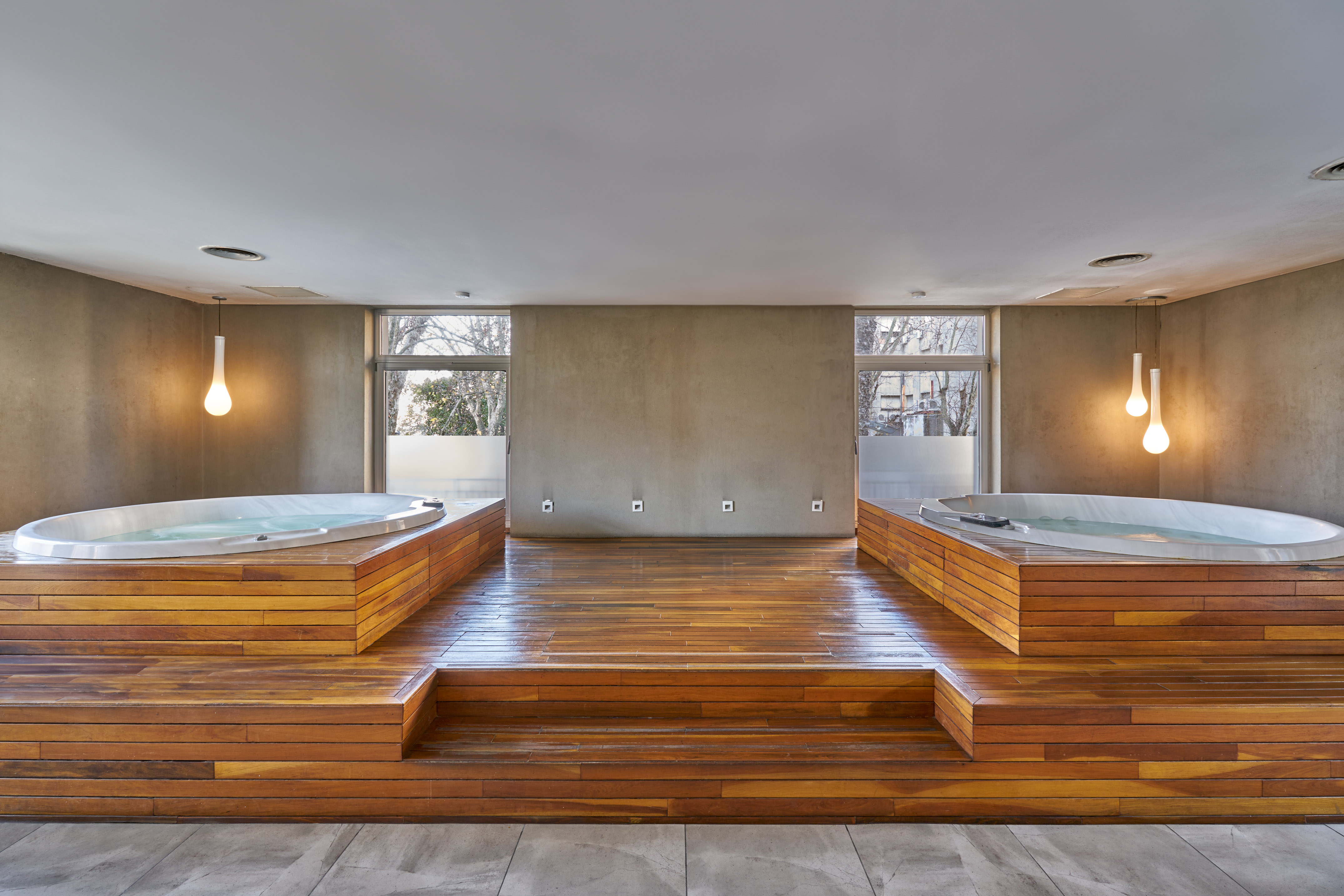 Twin white jacuzzis on polished wooden platforms in a modern spa room.
