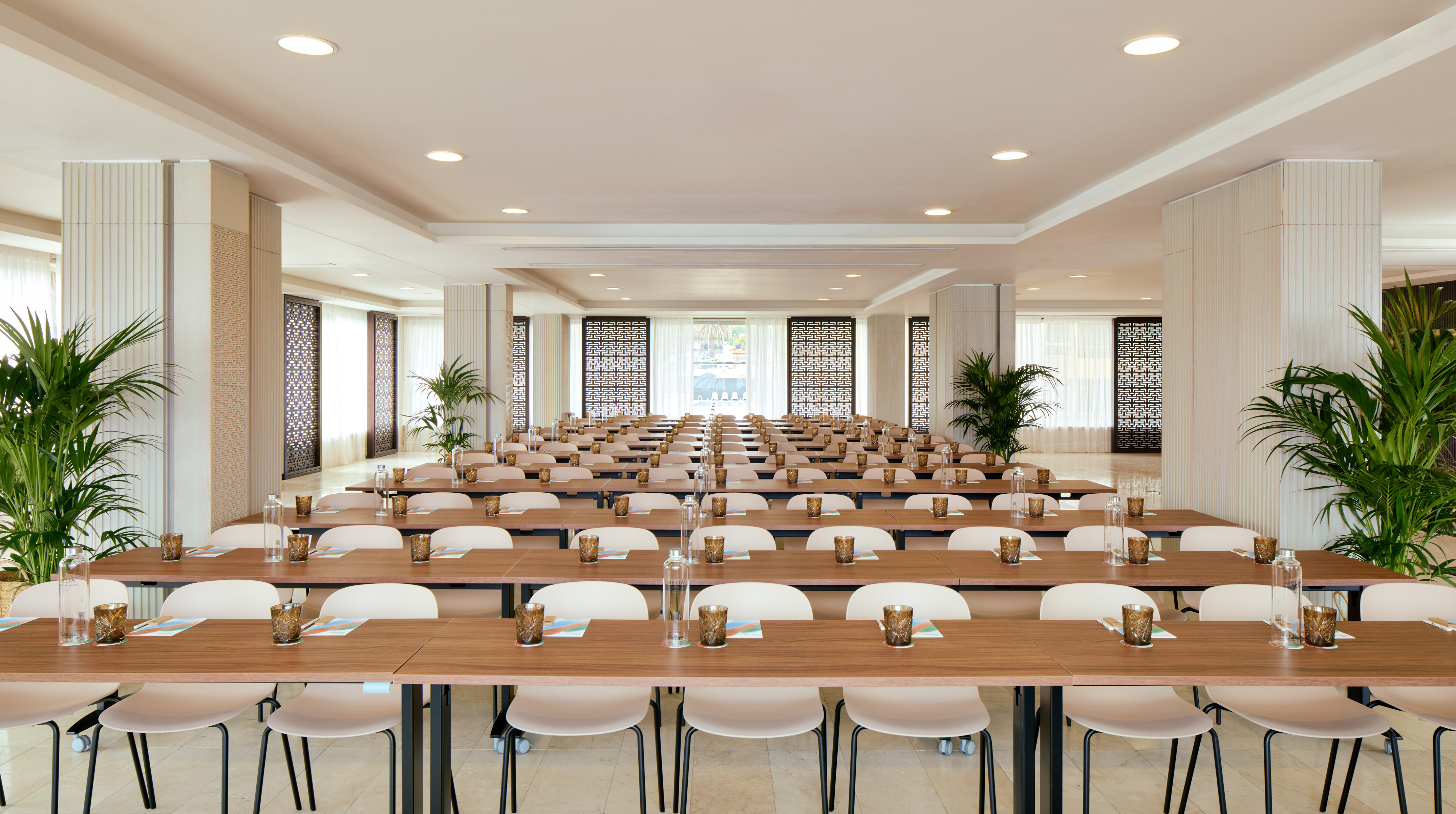 Bright conference room with neat tables, chairs, water, and green plants.
