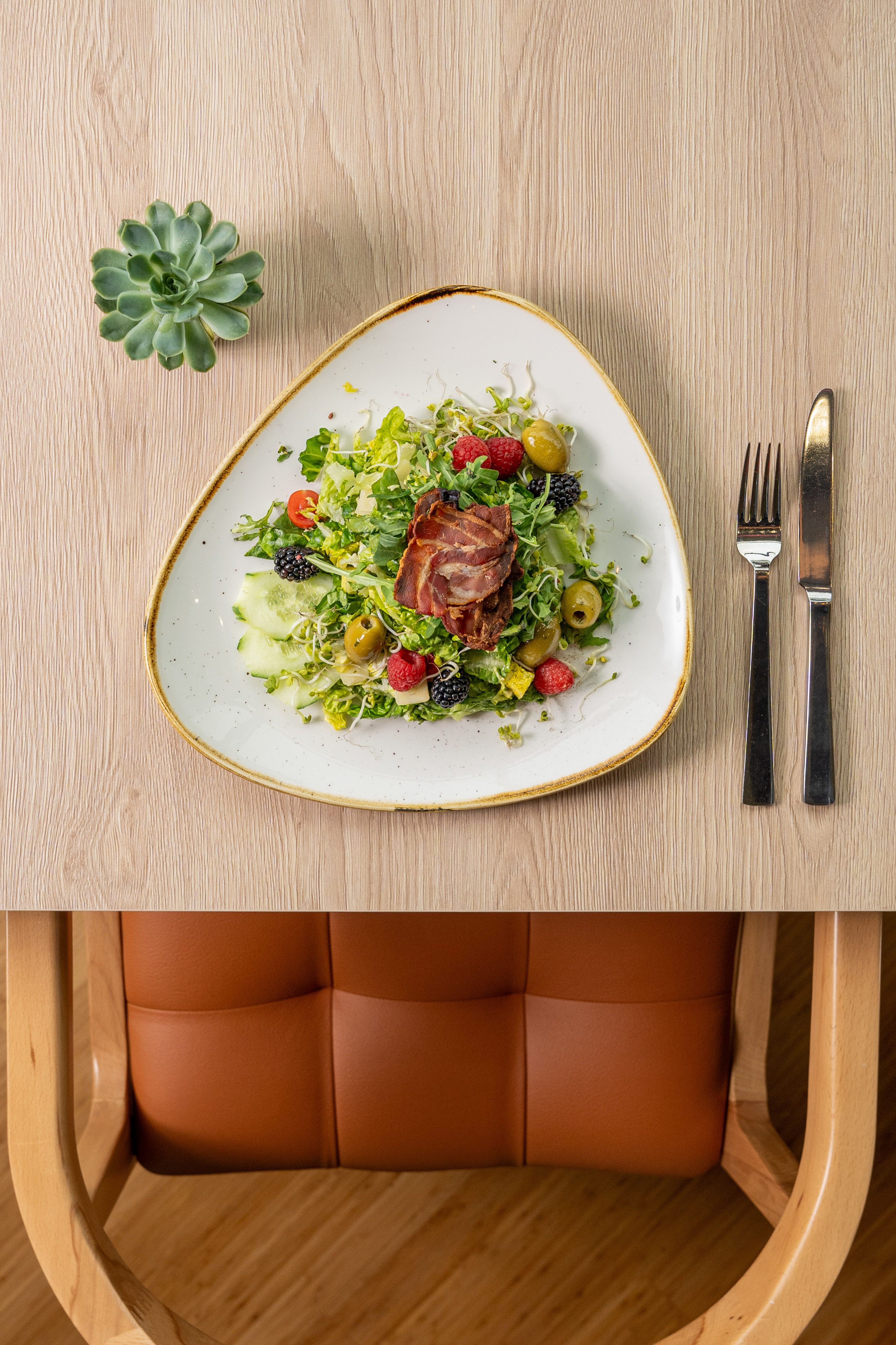 Fresh salad with crispy bacon, mixed berries, olives on a wooden table.