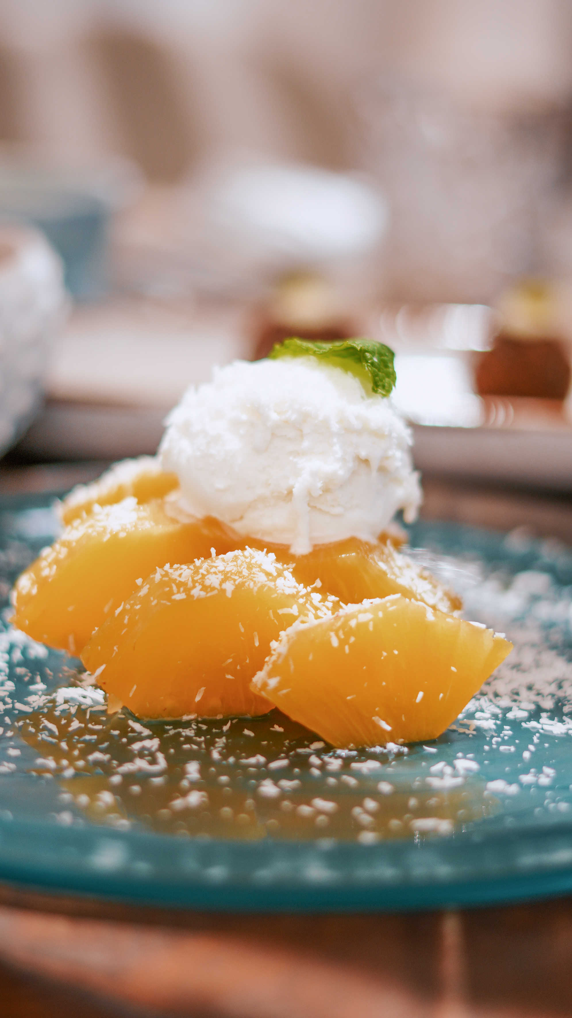 Dessert with orange fruit pieces, ice cream, coconut flakes, and mint garnish.